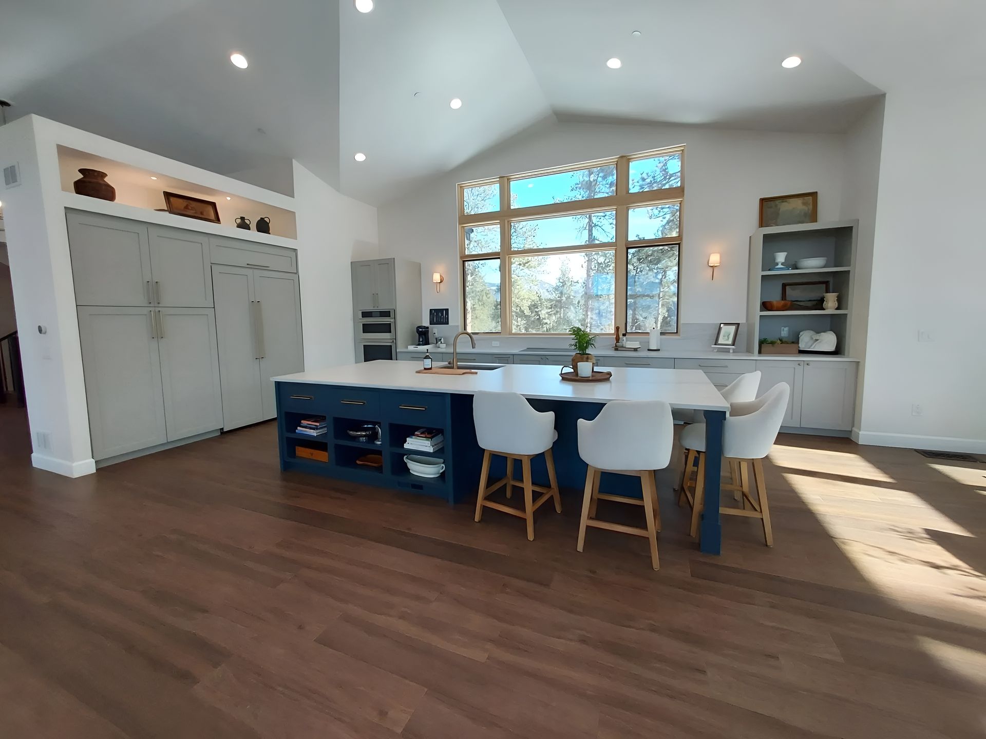 Modern kitchen with blue island, white countertops, wood floors, and large window with view.
