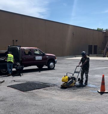 A man in a yellow vest is spraying asphalt in a parking lot