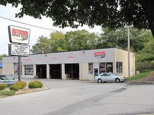 AutoCare service center with open bays, sign, and parked car on a sunny day.