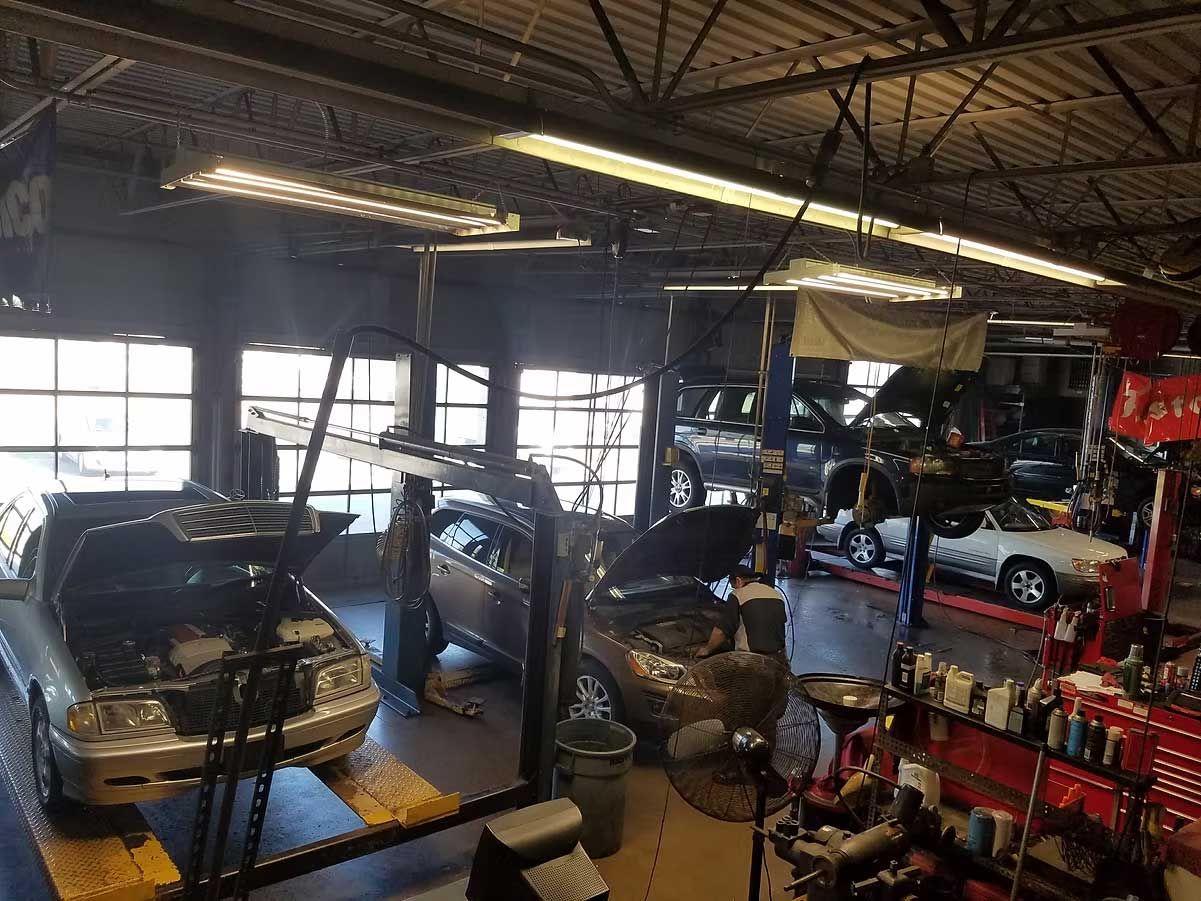 Auto repair shop interior: Cars on lifts, mechanic working, tools and equipment visible.