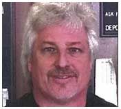 Man with graying hair and mustache smiling, indoors near a sign.