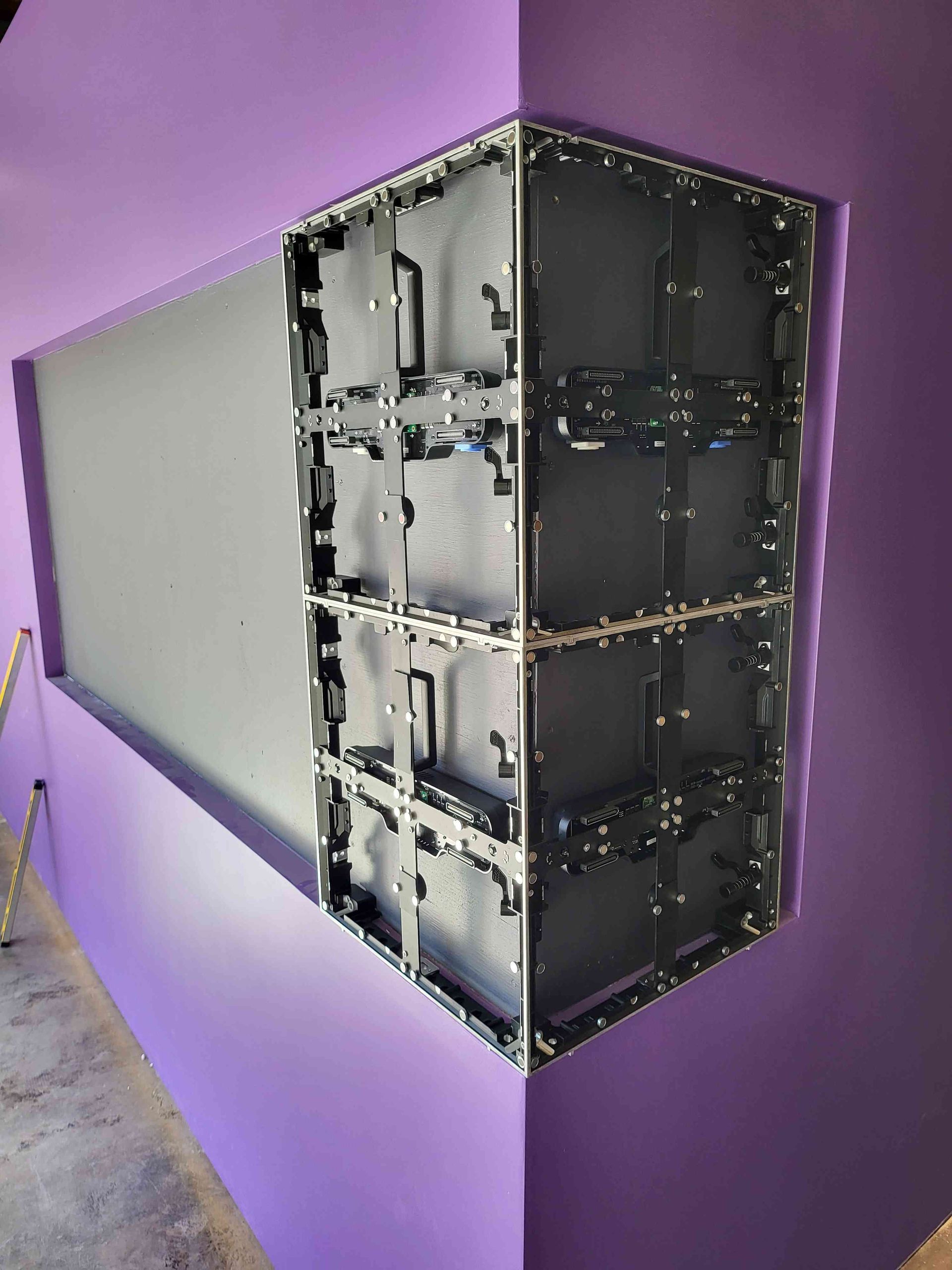 A large video screen installed in a corner, with the back revealing the internal components. Purple walls.