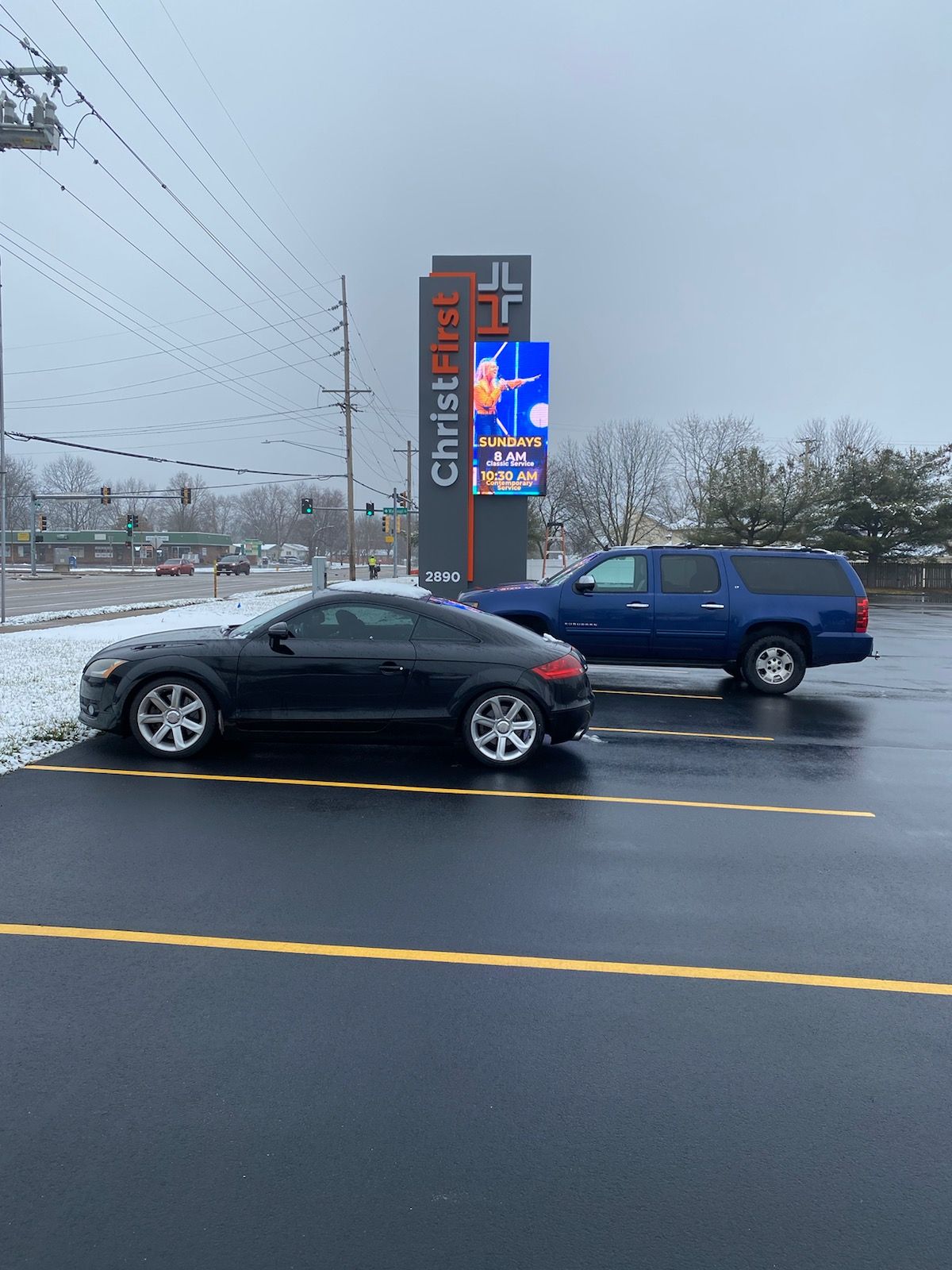 Black Audi TT in front of Christ Church sign, blue SUV, overcast day, snow on the ground.