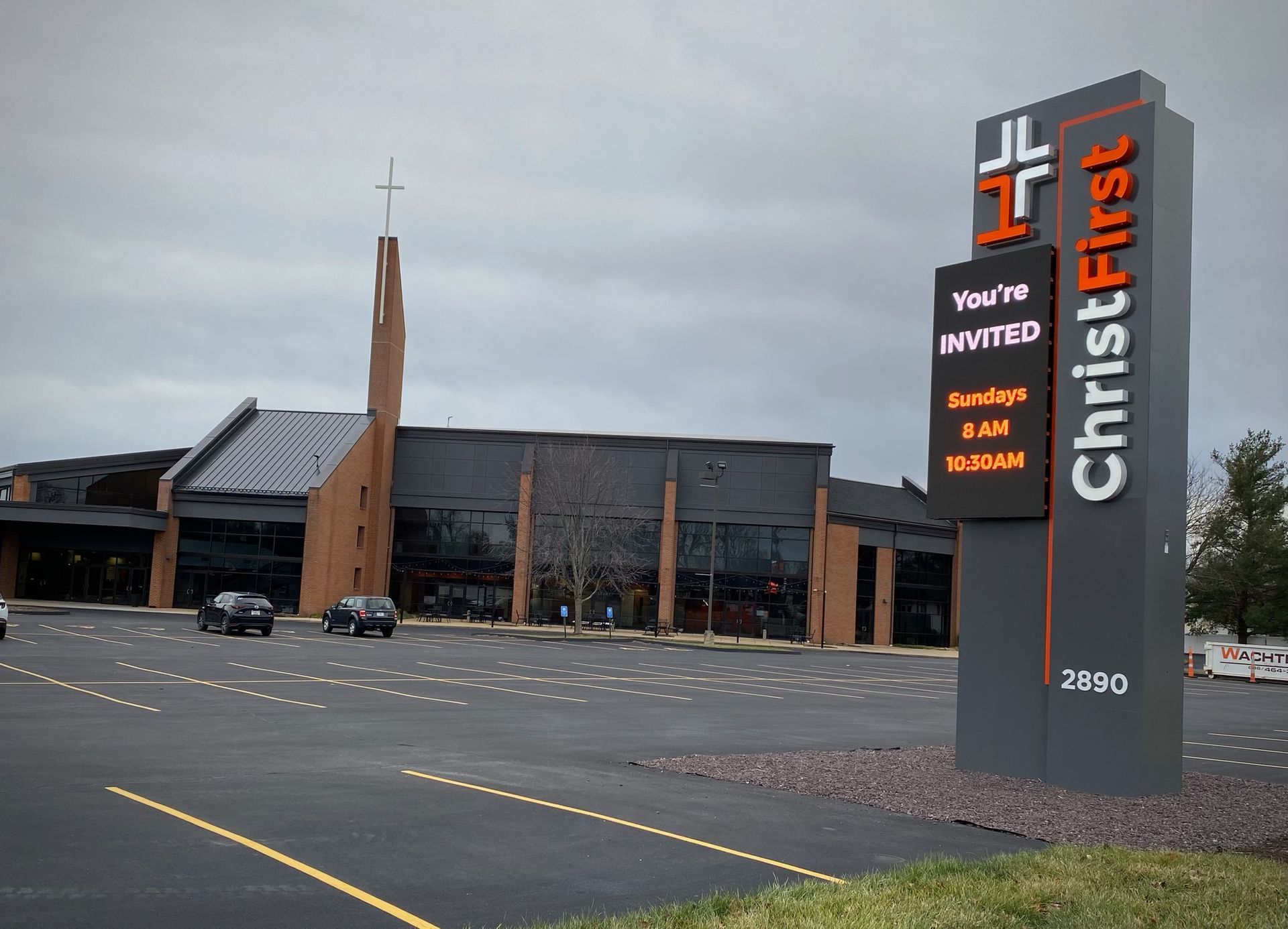 ChristFirst church exterior with sign. Building: gray/black, cross on steeple. Sign: orange/white text.