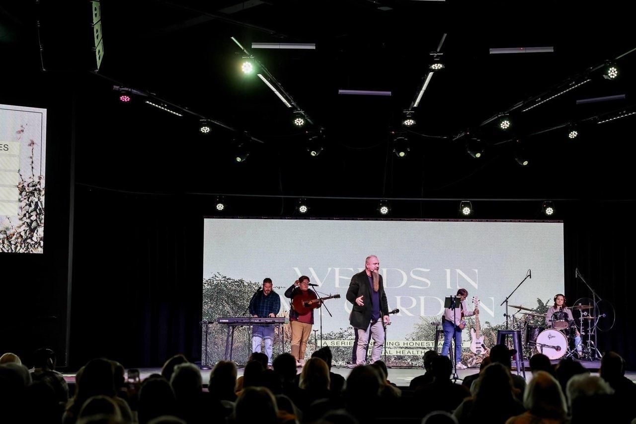 Band performing on stage in front of a crowd. Stage has a large screen with text 