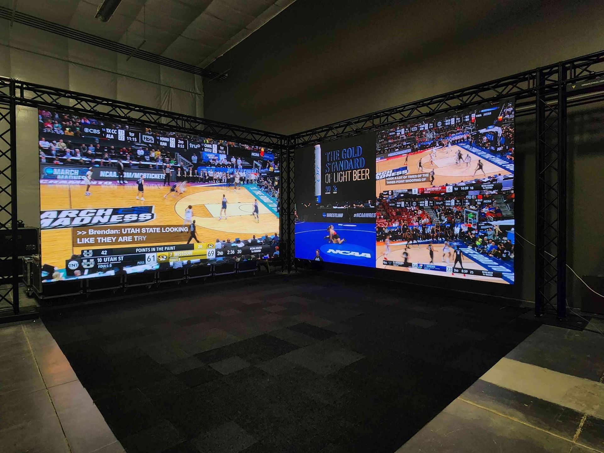 Two large video screens inside a dark room showing a basketball game.
