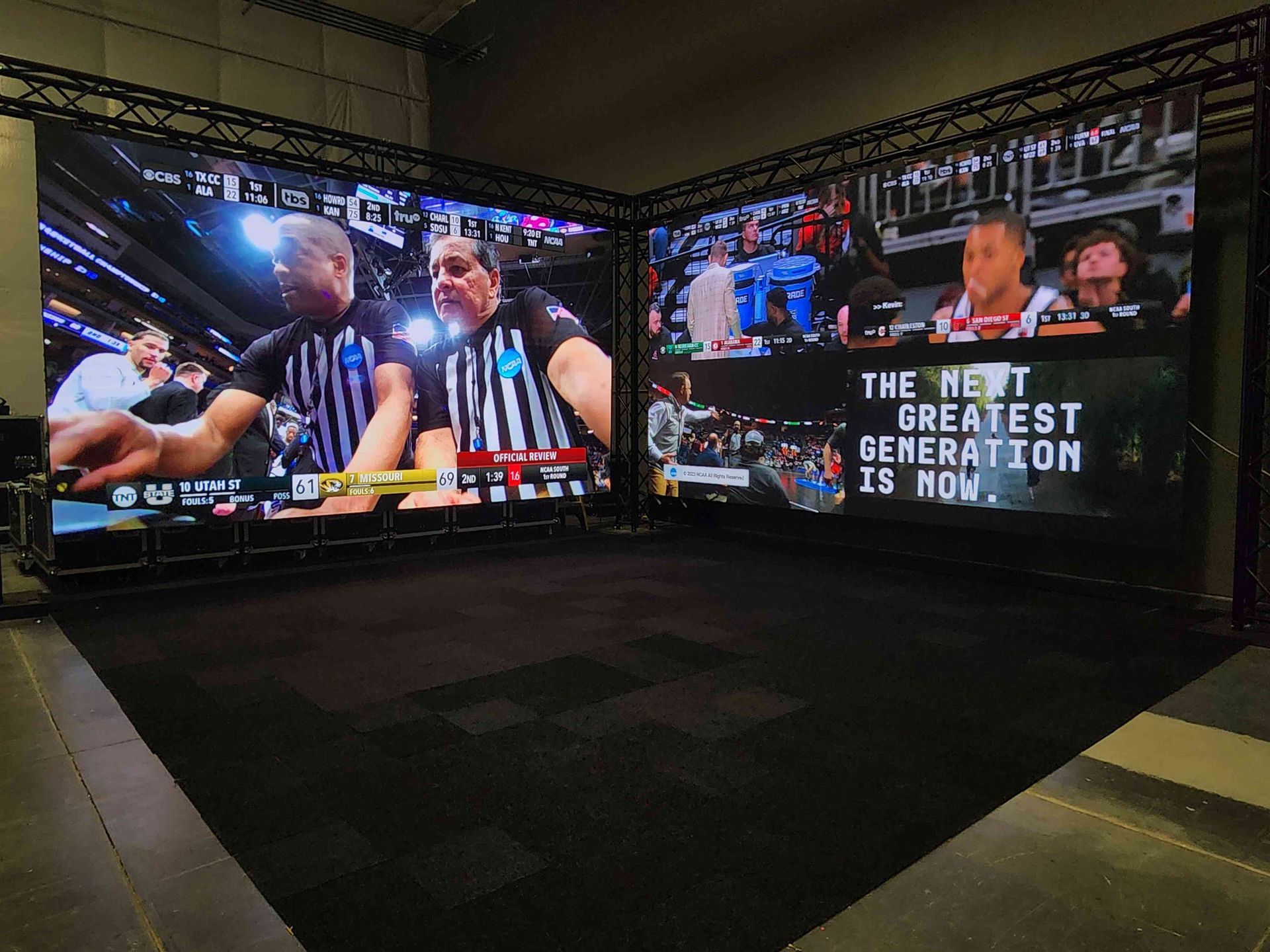 Two large video screens displaying sports footage, set up in a dark, indoor space.