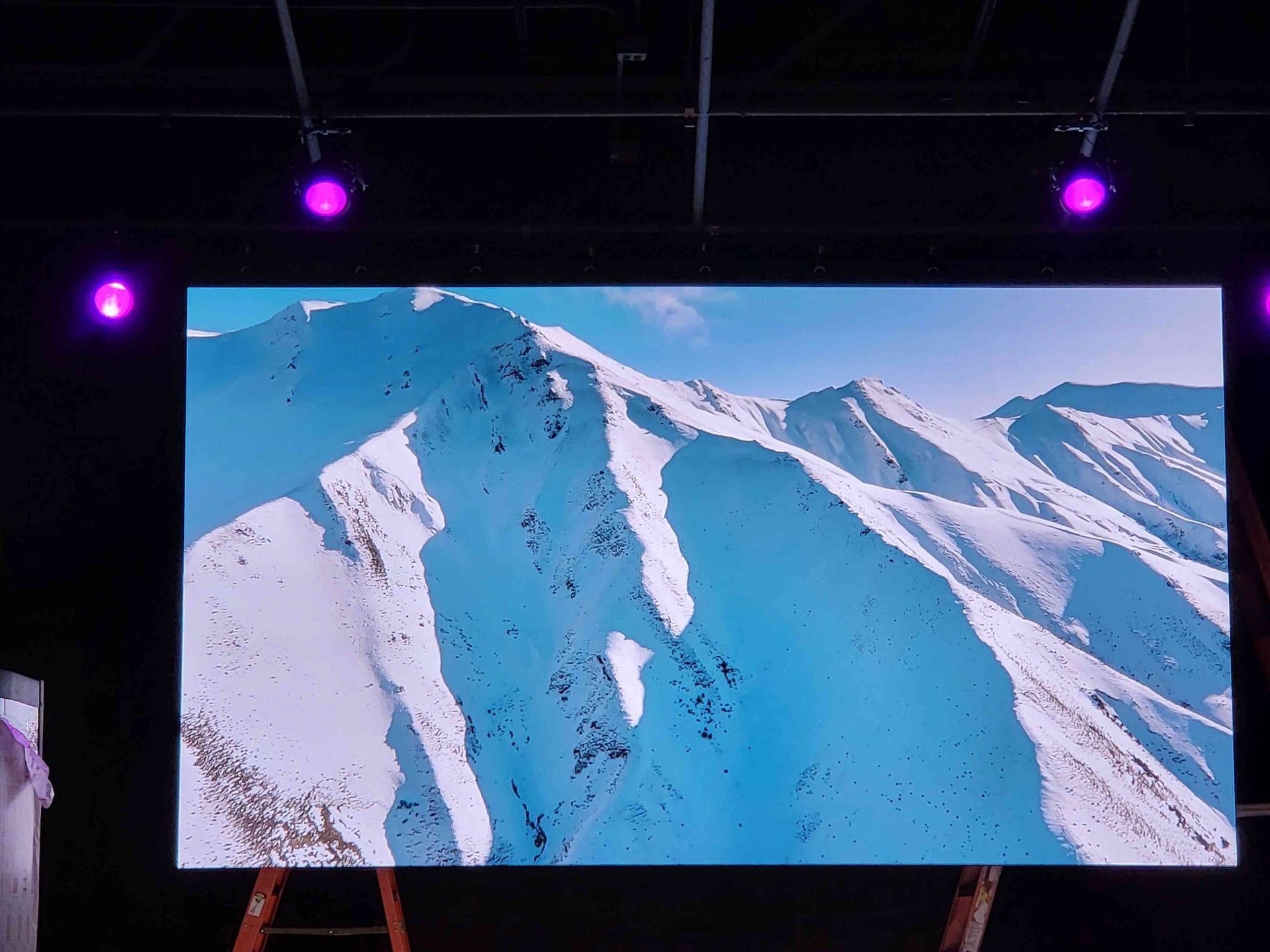 Large screen displaying a snowy mountain scene, with purple lights overhead.