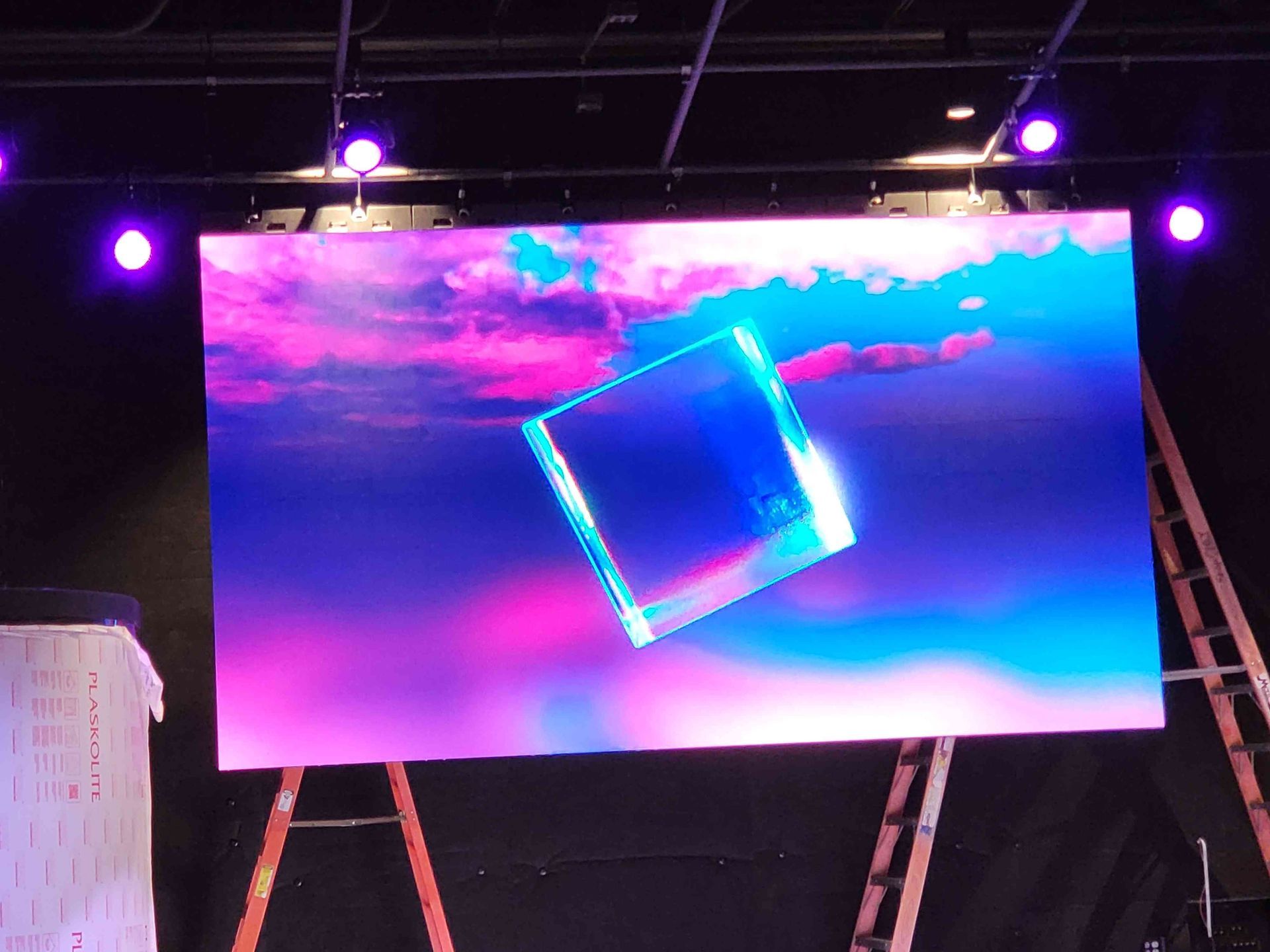 Large screen displaying a vibrant abstract scene with a floating, glowing cube against a pink and blue sky.