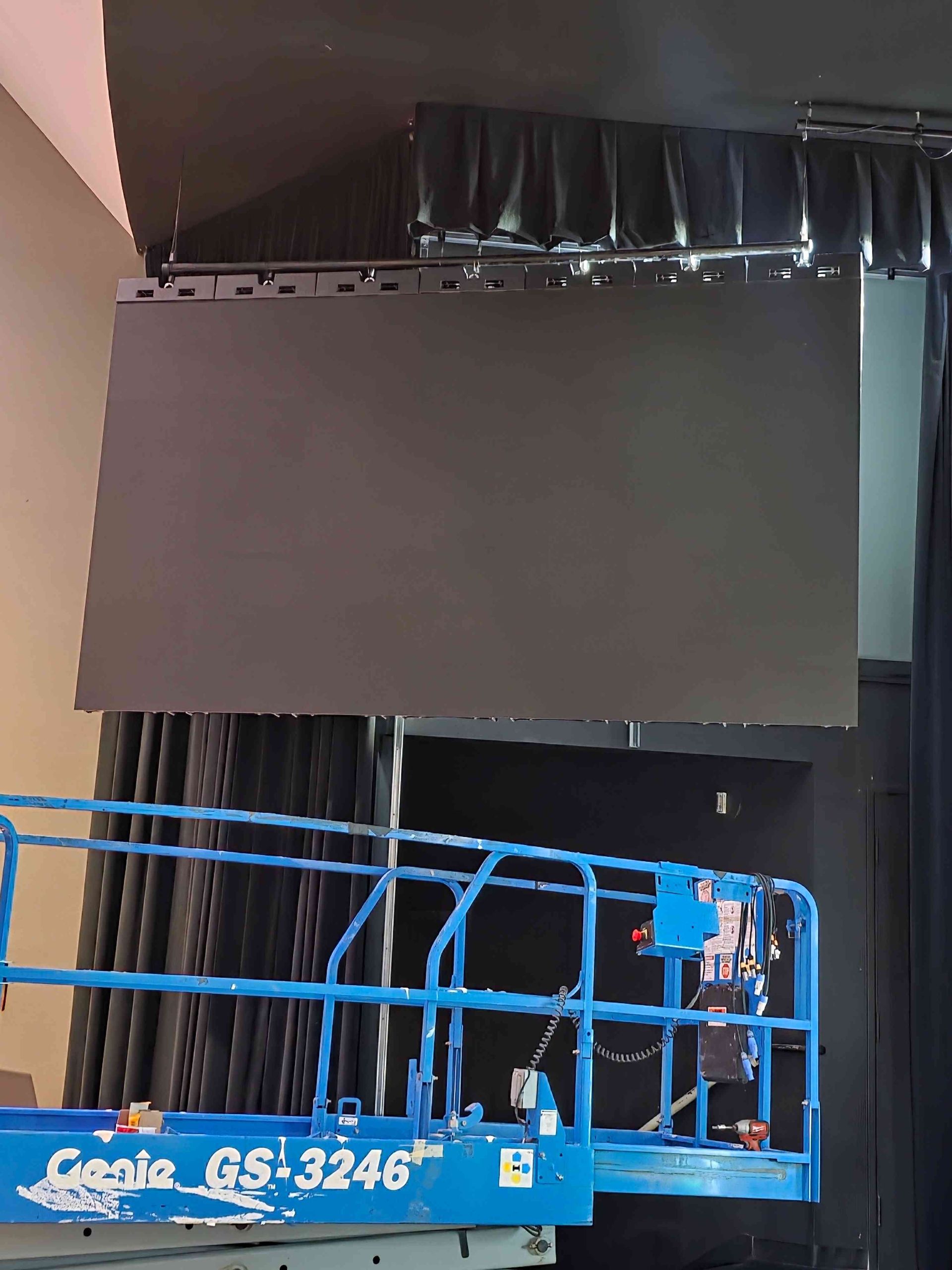 A large, black LED screen suspended above a blue lift, installed on a stage.