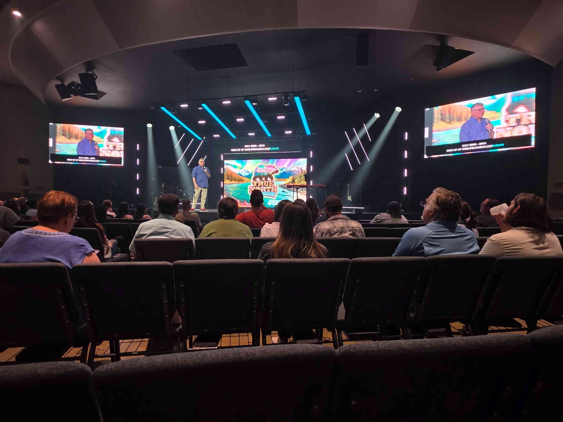 Audience in church watching a presentation on stage with bright lights and screens.