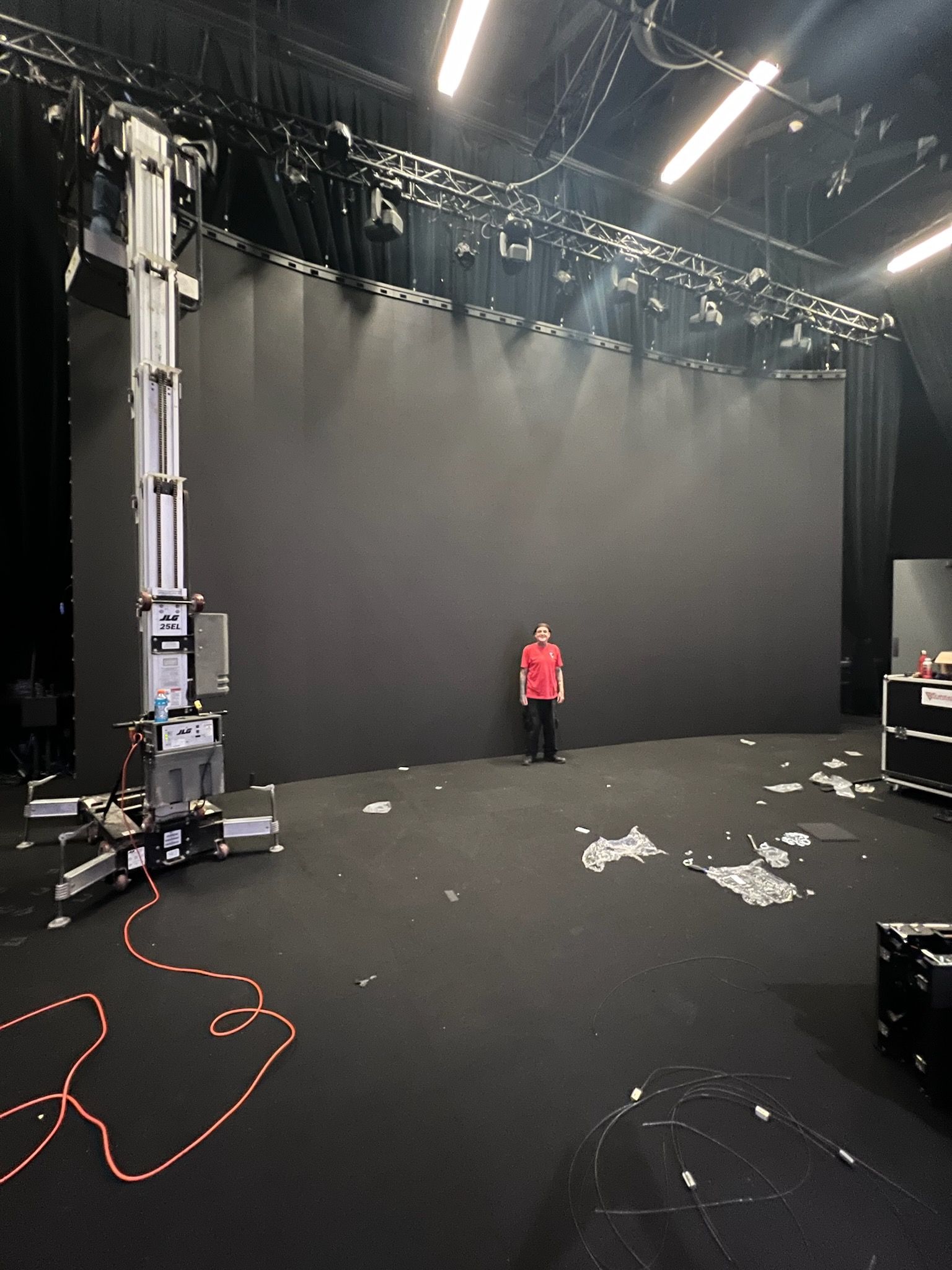 A person stands before a massive black screen in a studio. Equipment surrounds them, wires on the floor.