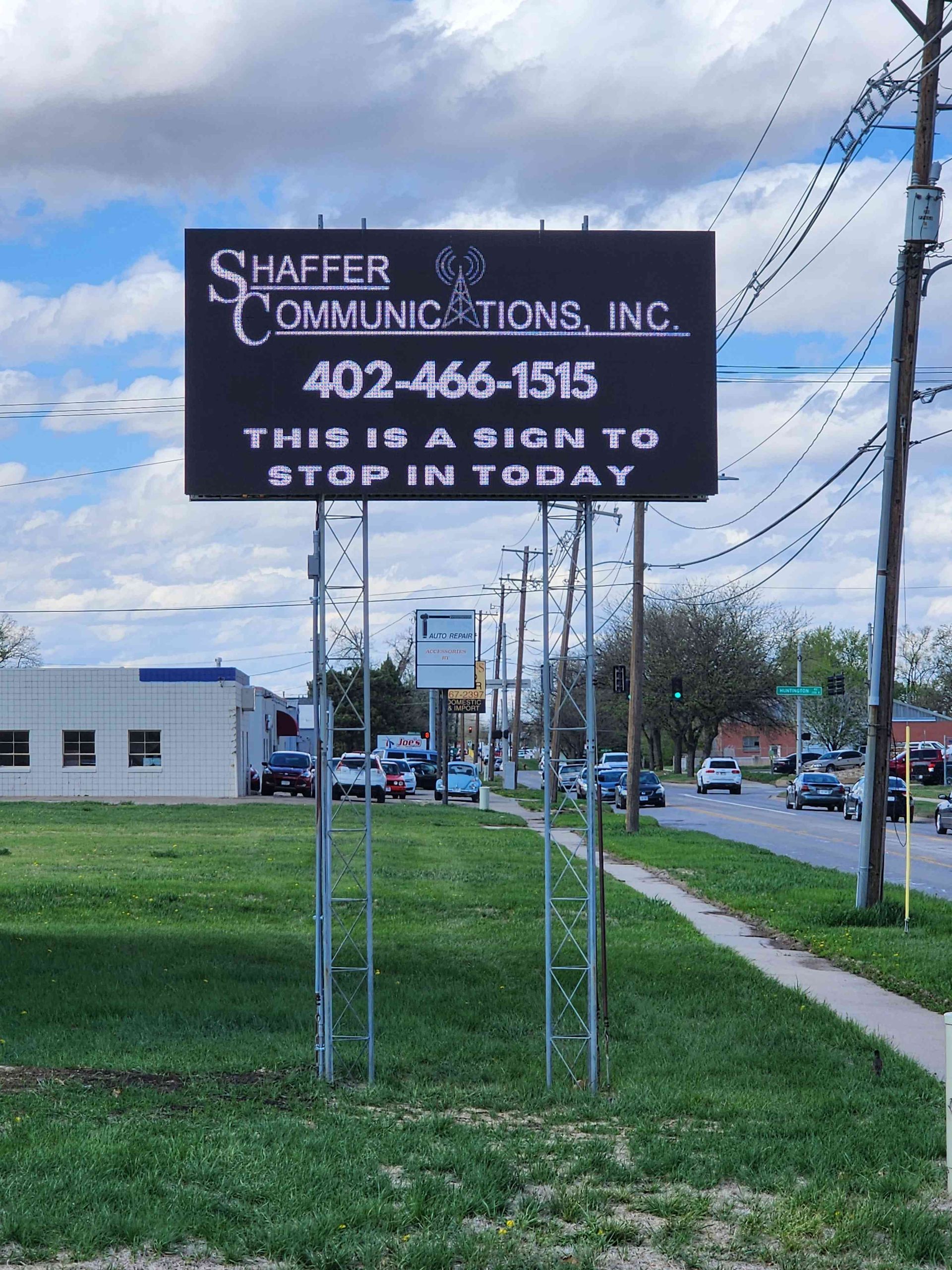 Digital billboard with Shaffer Communications, Inc. info and call to action, 402-466-1515, green grass, and street in background.