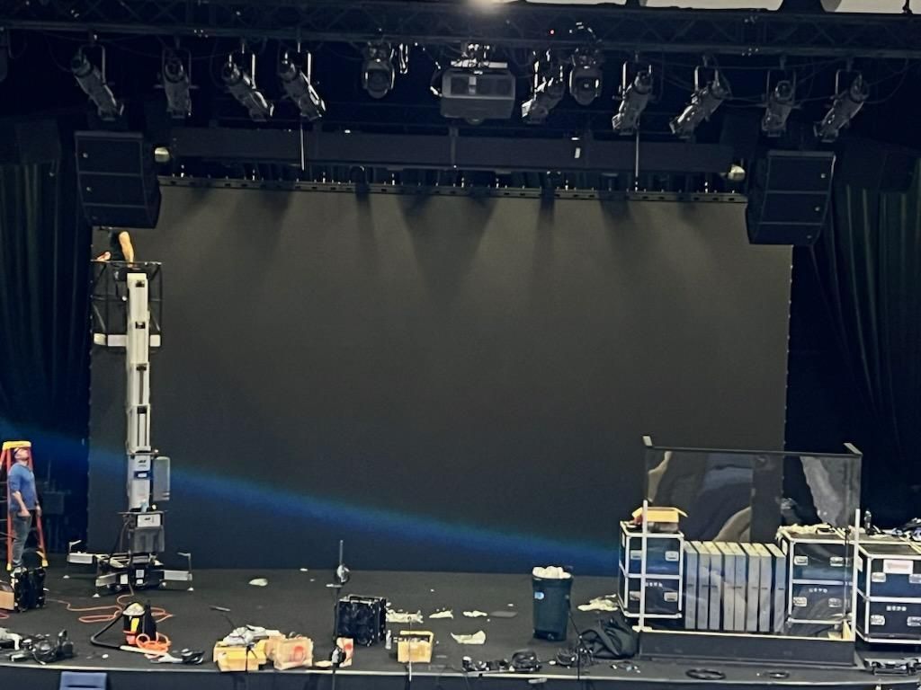 Stage setup with lights, speakers, a large screen, and equipment. A person is on a lift.