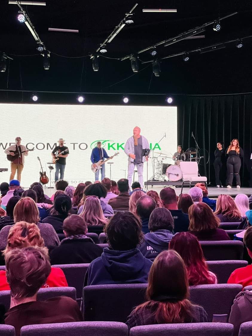 Audience watching a band perform on stage with a green backdrop. 