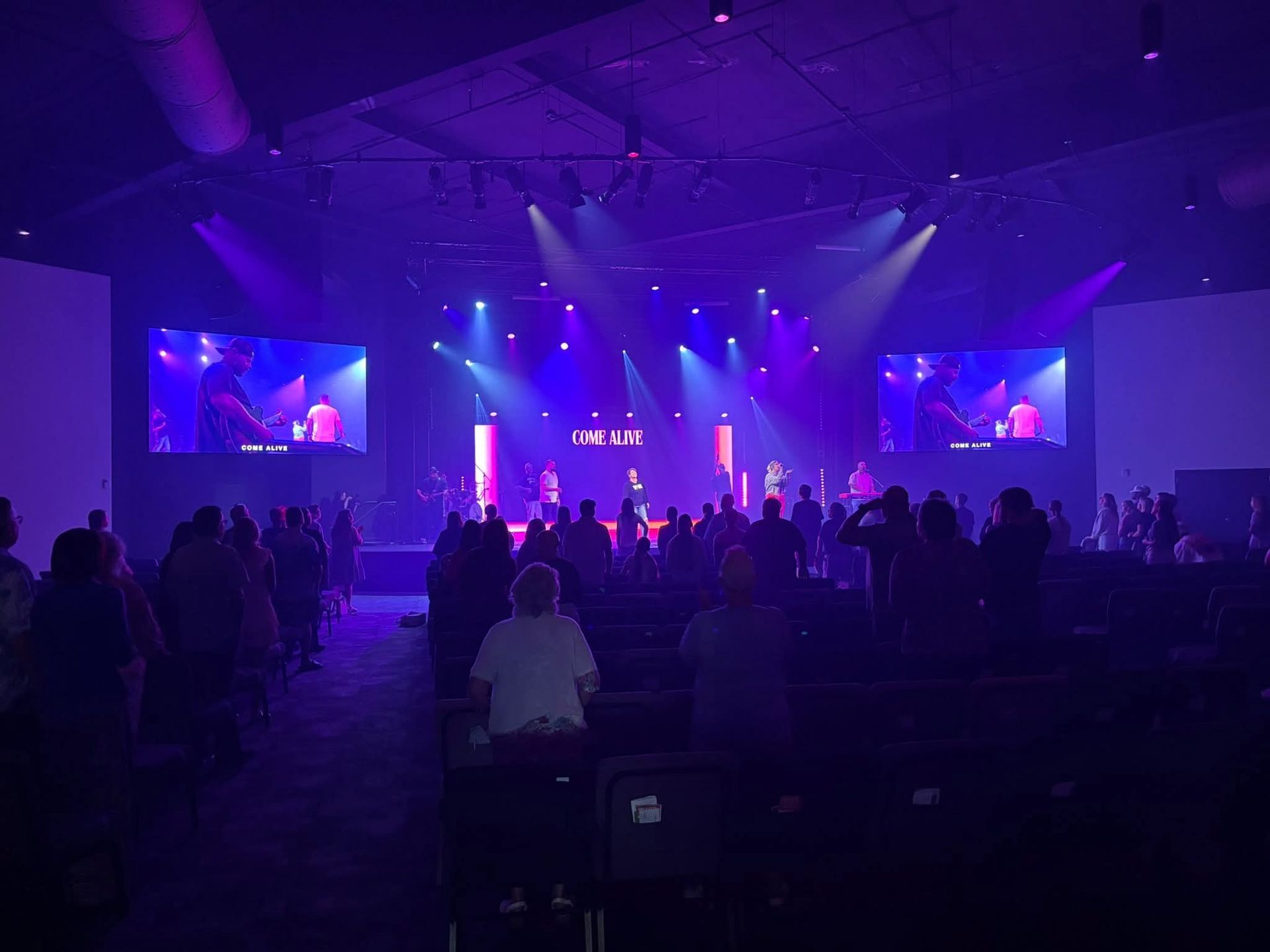 Audience in a church watching a performance on stage under purple lights.