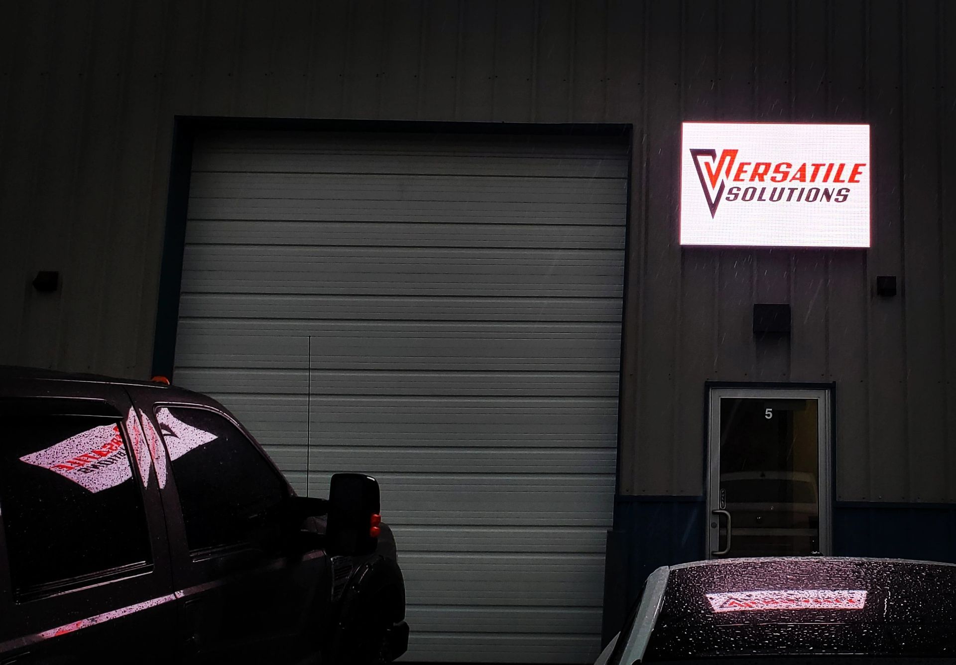Sign for Versatile Solutions above a garage door; dark truck in the foreground.
