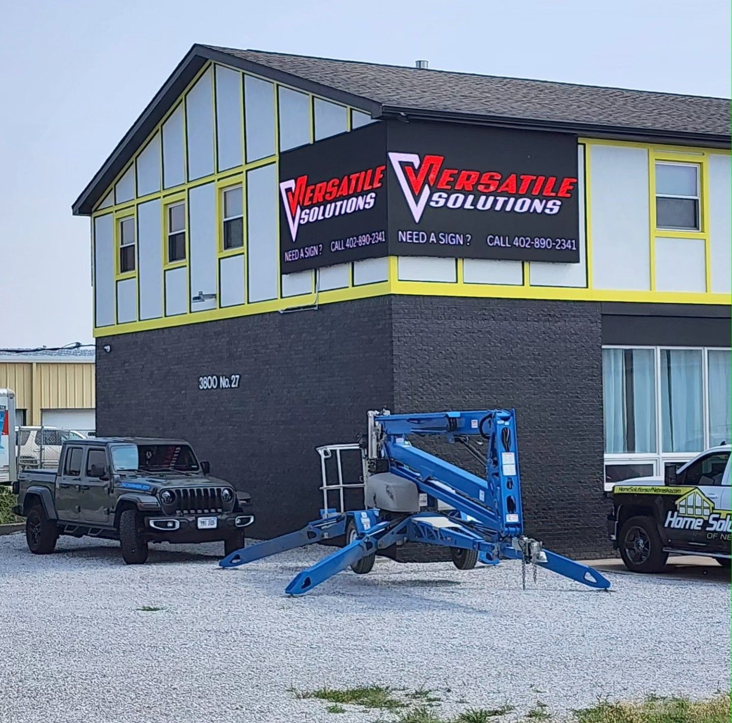 Versatile Solutions building with banner, blue lift, black truck, and a Jeep parked outside.