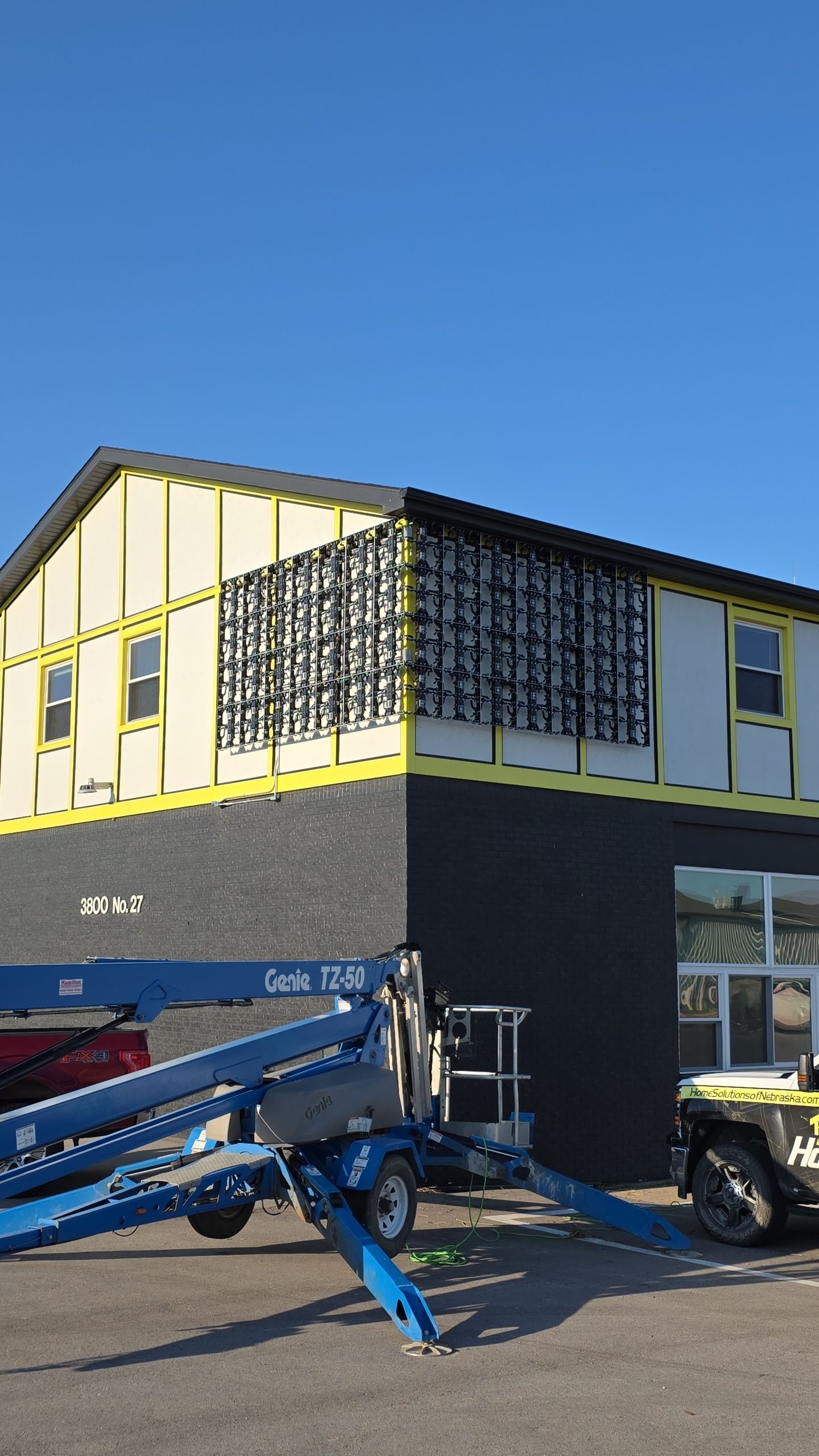 Building under construction, black facade, yellow trim, blue lift, clear sky.
