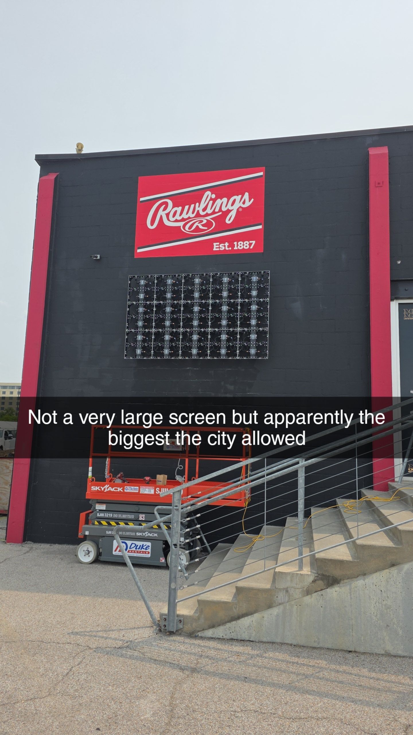 Rawlings sign on a black building with a small digital screen; an orange lift and stairs in front.