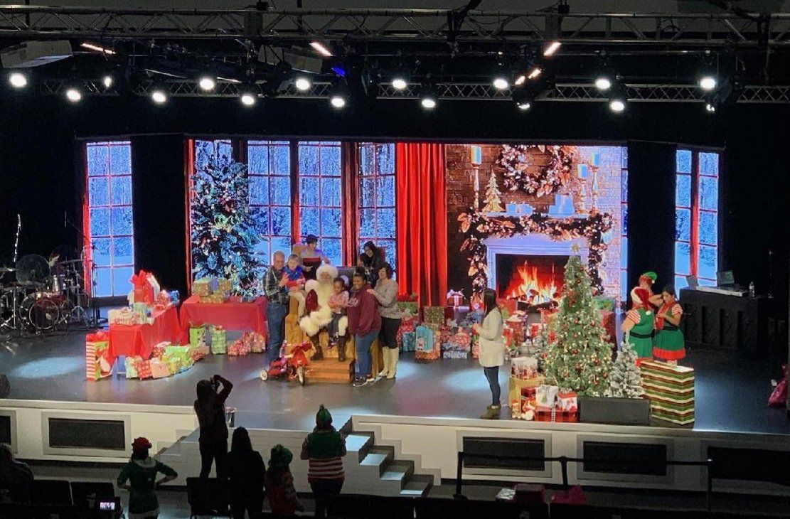 Christmas stage with performers, presents, and festive decor. People gather with Santa.