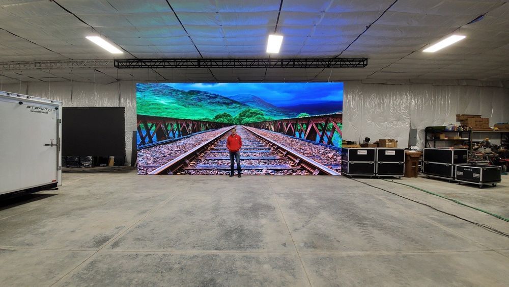Person standing before a large LED screen displaying a landscape in a warehouse.
