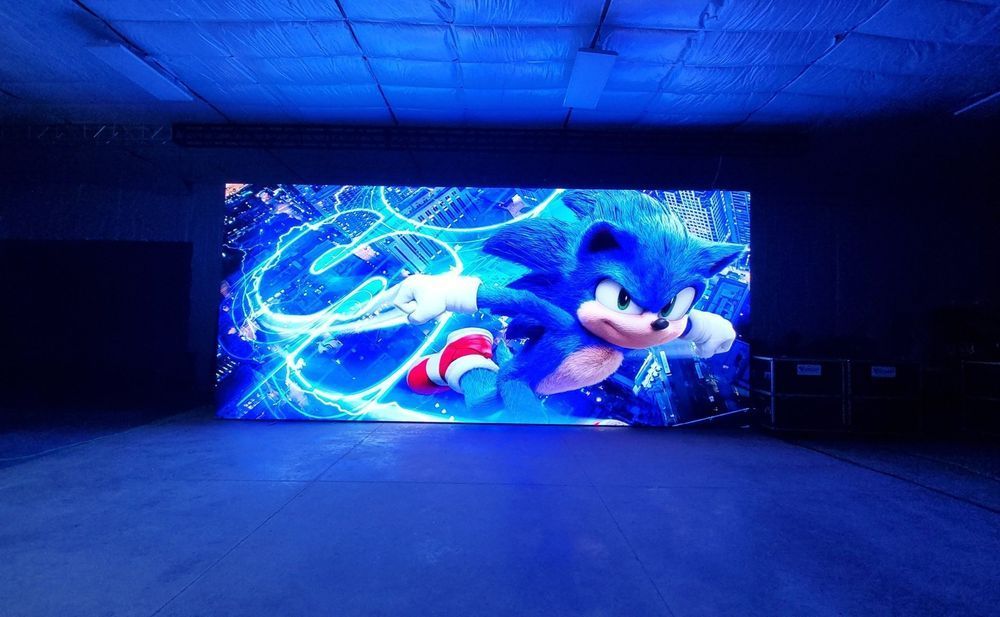 Sonic the Hedgehog on a large blue screen in a dark room, surrounded by blue lighting.