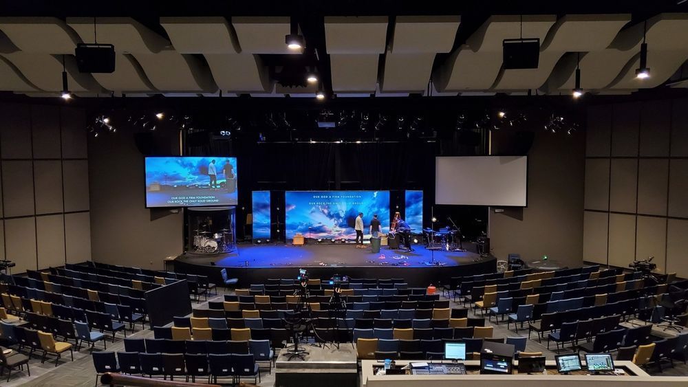 Auditorium with stage, band, and screens; rows of seats face the stage.
