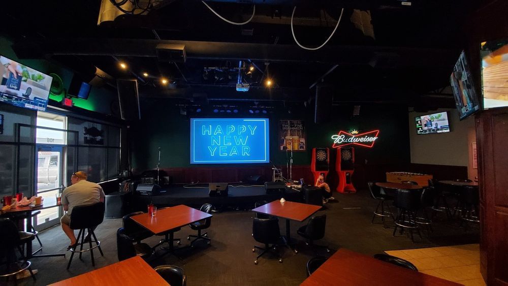 Interior of a bar with tables, a stage, and TVs. 