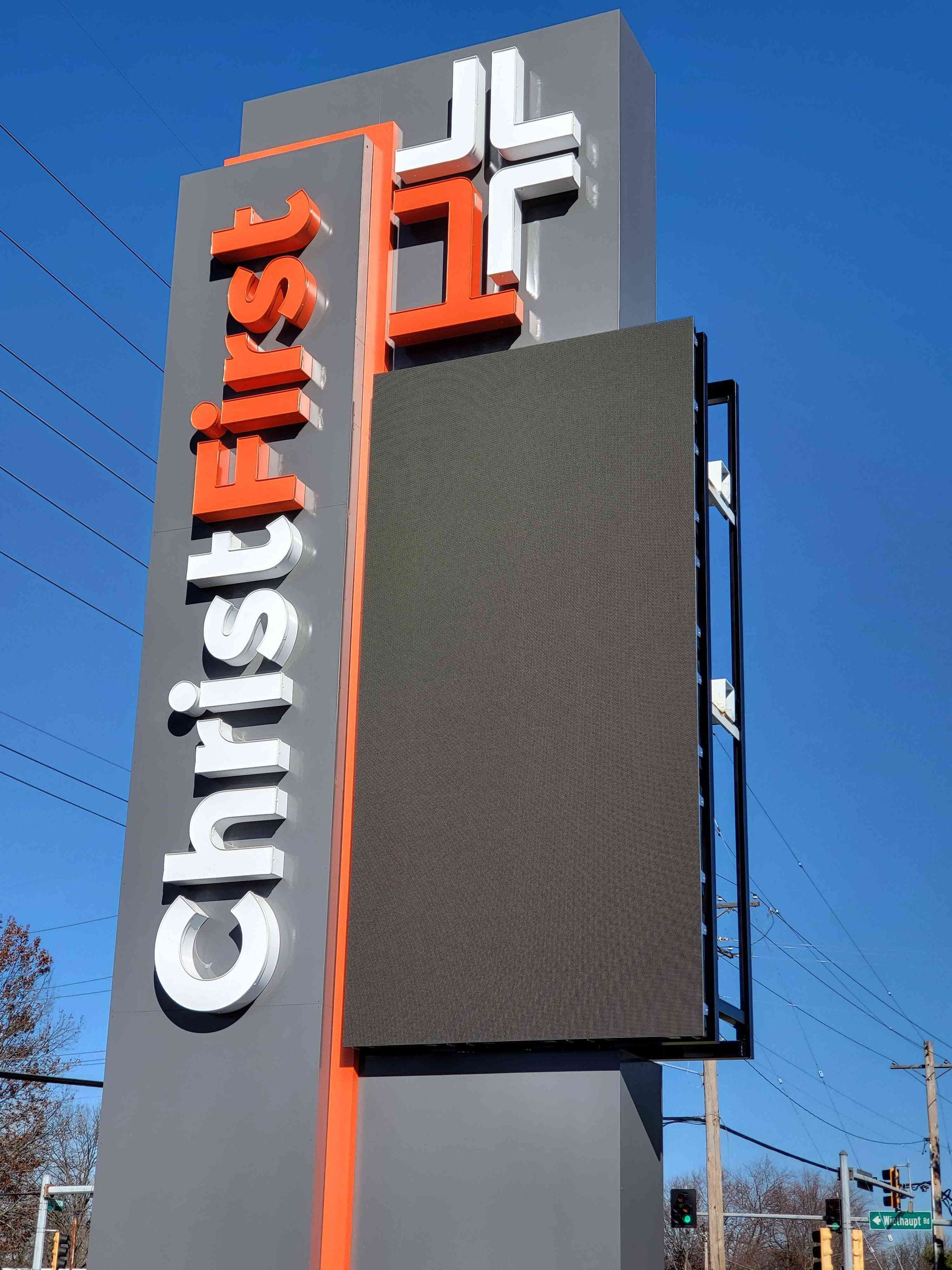 Sign for First Christ Church, with an LED display screen. Gray and orange with a white cross and text.