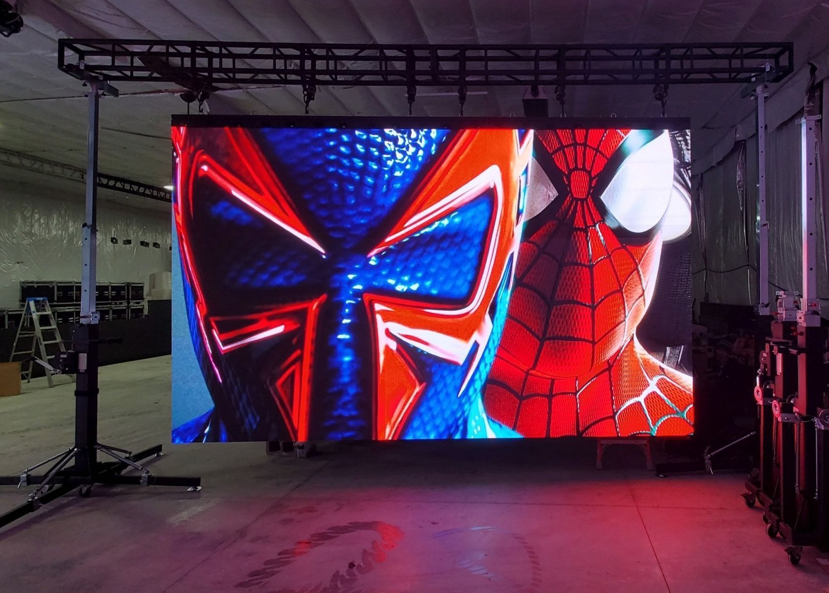 Spider-Man characters on a large LED screen, suspended in a warehouse setting with rigging.