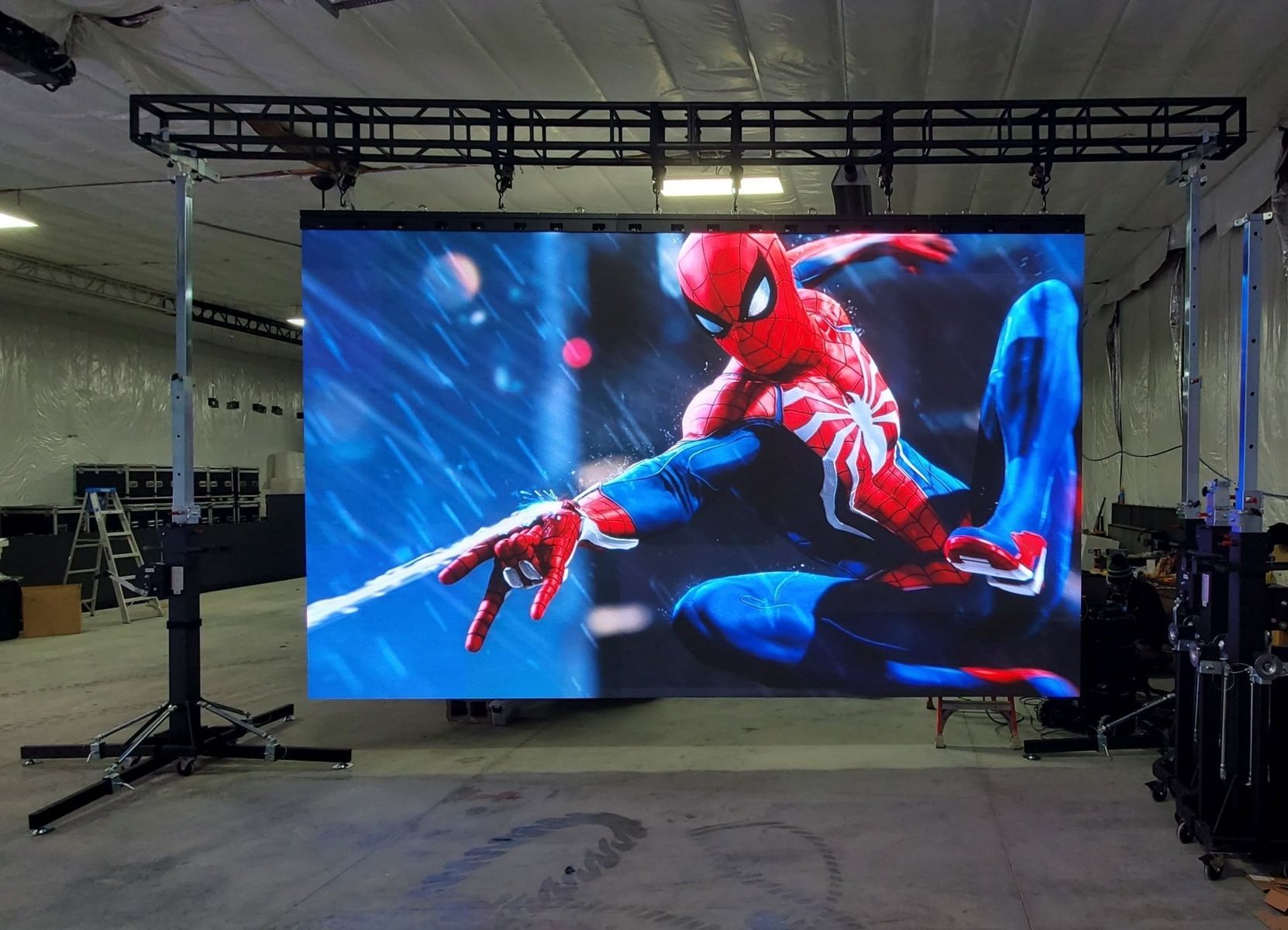 Spider-Man on a large LED screen with a metal truss structure indoors.