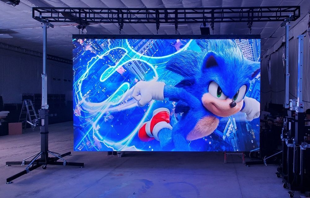 Sonic the Hedgehog on a large LED screen, lit with blue hues, in a studio with black trusses.