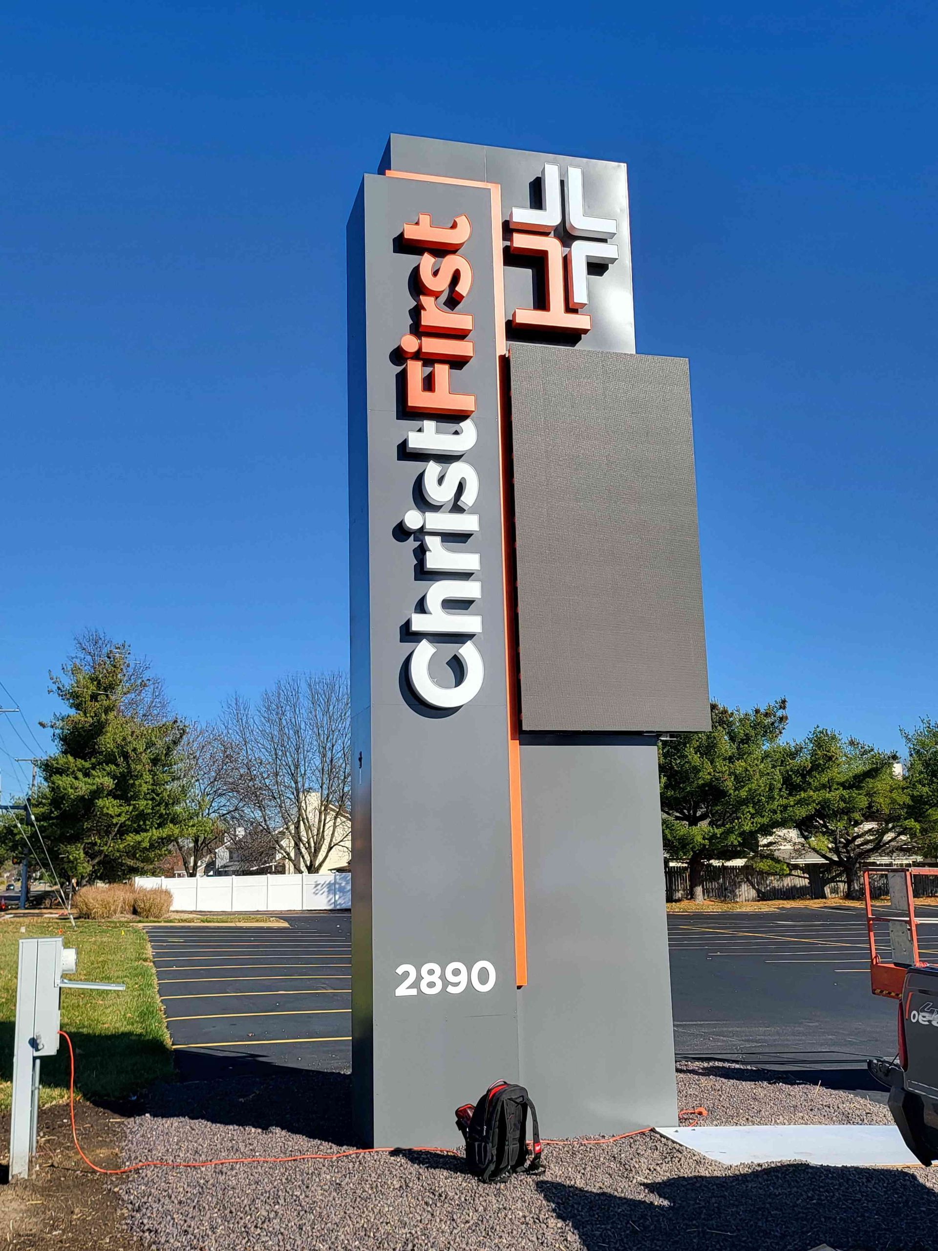 Sign for ChristFirst church at 2890. Tall gray structure with orange and white text, cross emblem, and a digital display.