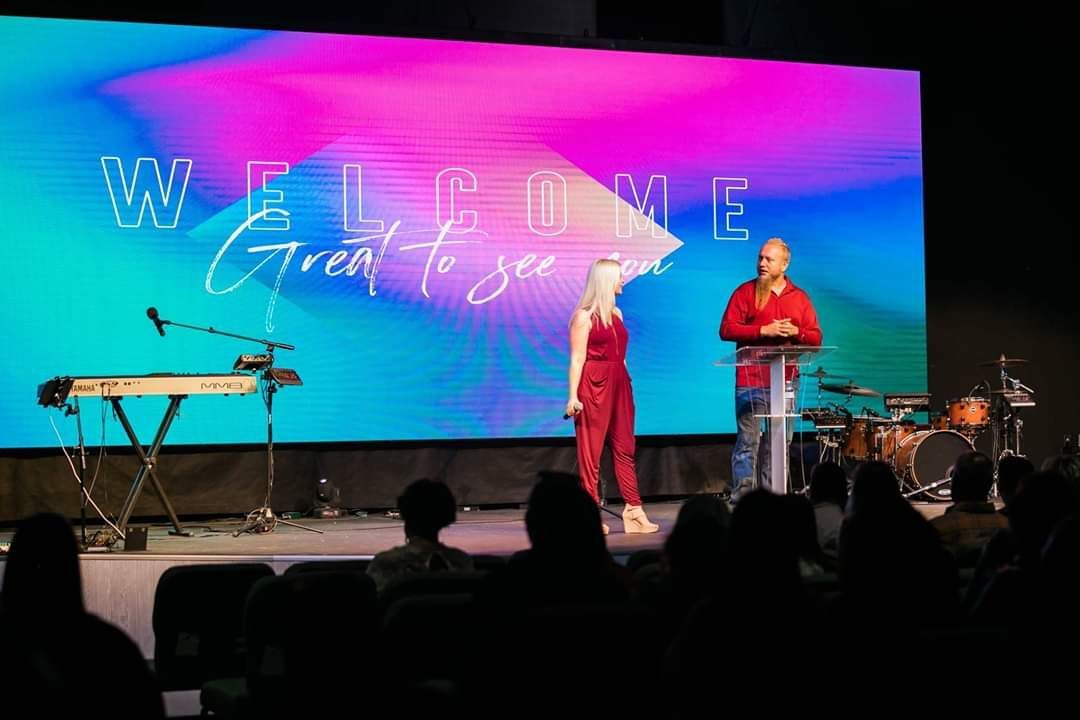 Two people on stage in front of a screen with 