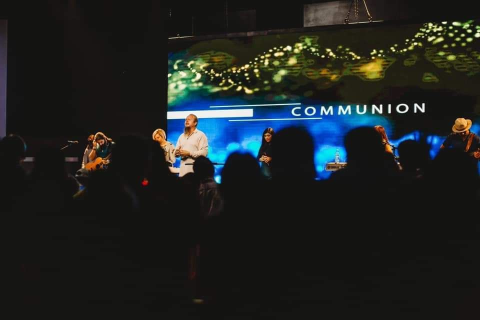 People taking communion in a church service.  A screen displaying the word 