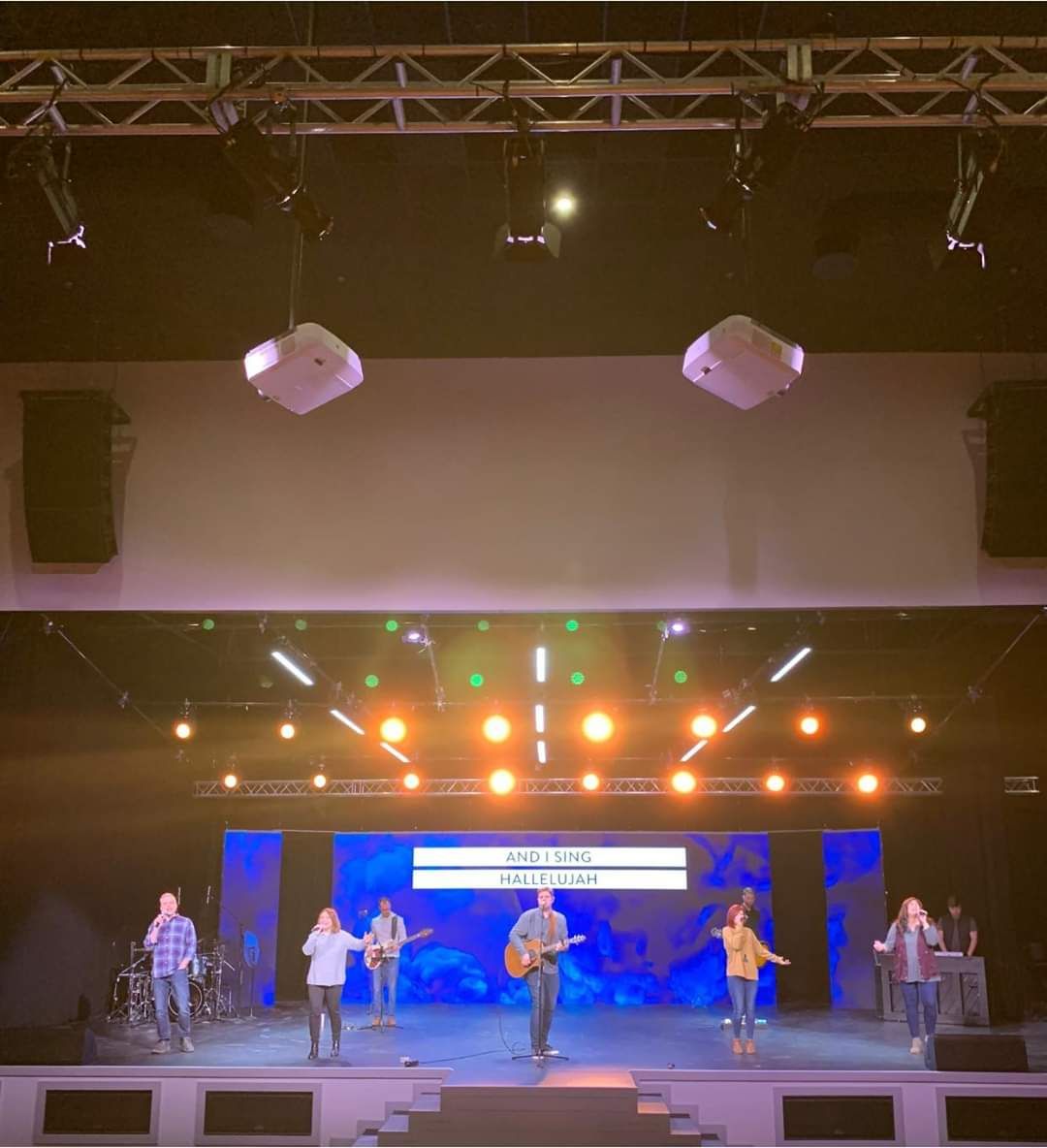 A band performs on stage with colorful lights. Musicians sing and play instruments.