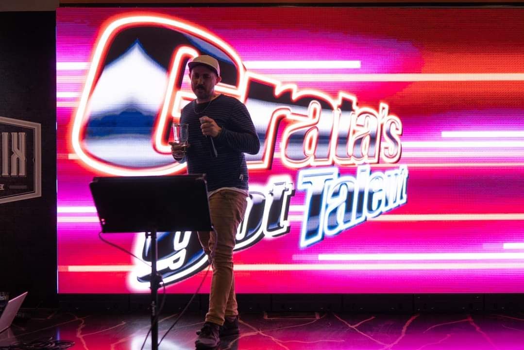Man on stage in front of a “India's Got Talent” backdrop, holding a microphone.