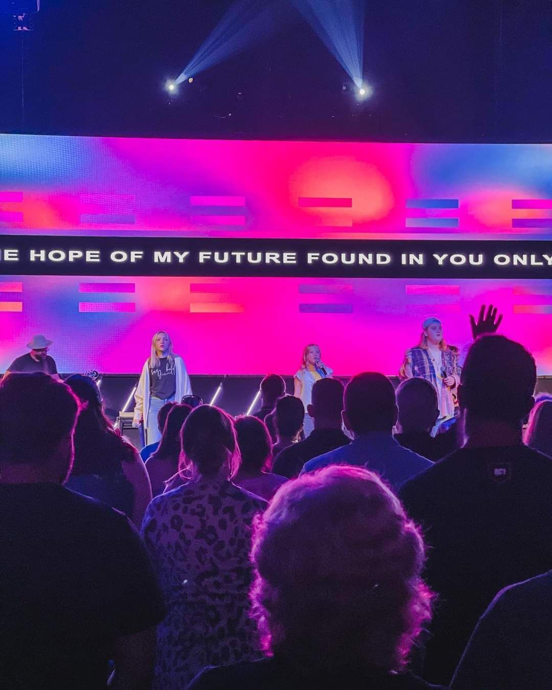 Church service: Band on stage with colorful backdrop; audience watching. Text: 