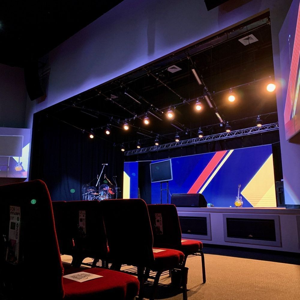 Empty auditorium stage with chairs facing it, with a colorful display and stage lighting.