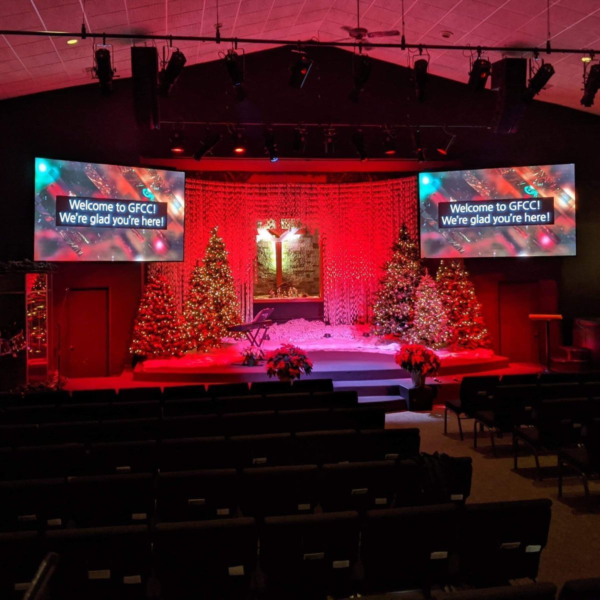 Christmas-decorated stage in a church with screens saying, 