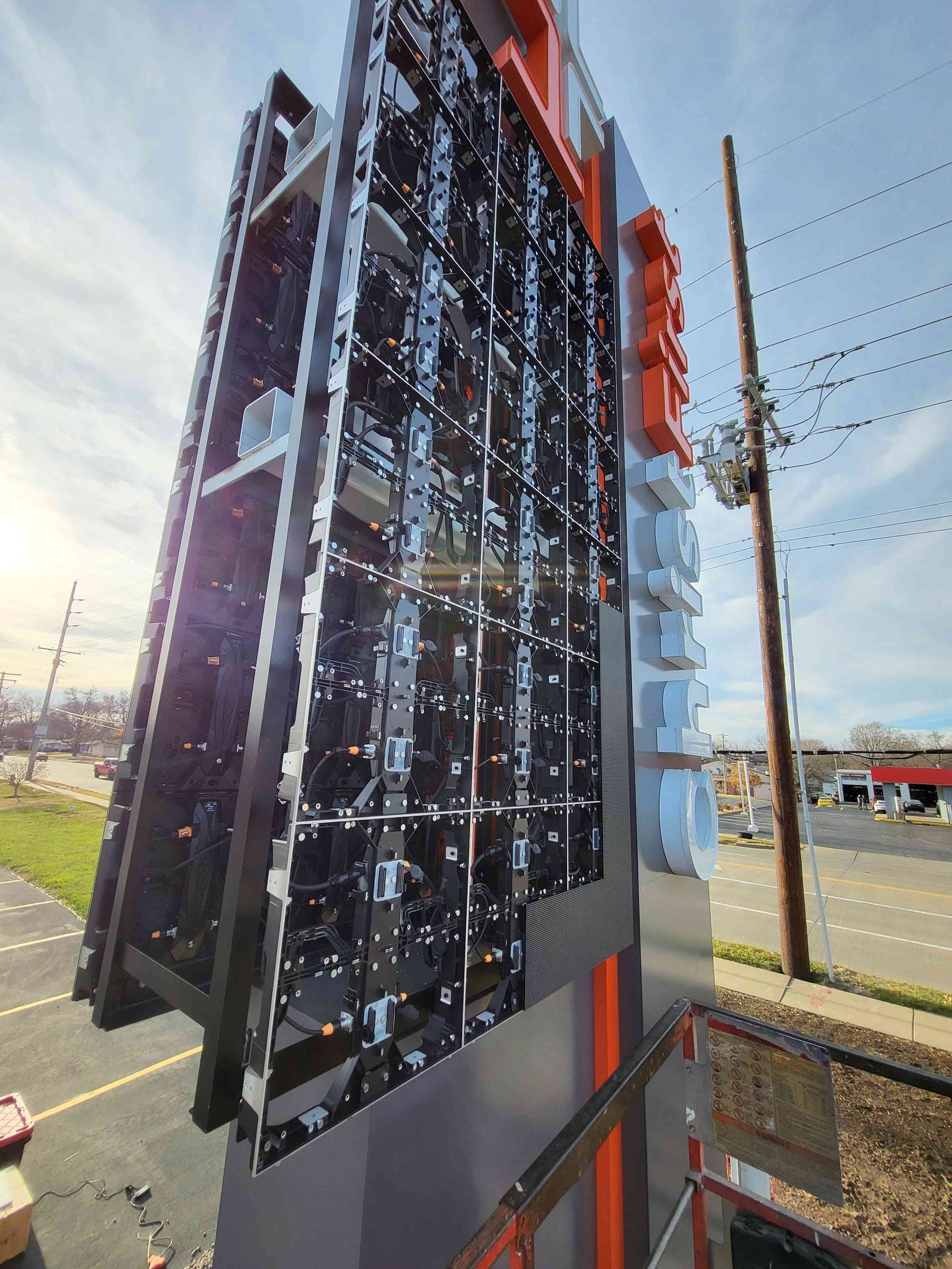 Close-up of a large, modern billboard with black panels, silver frame, and red/white lettering in an outdoor setting.