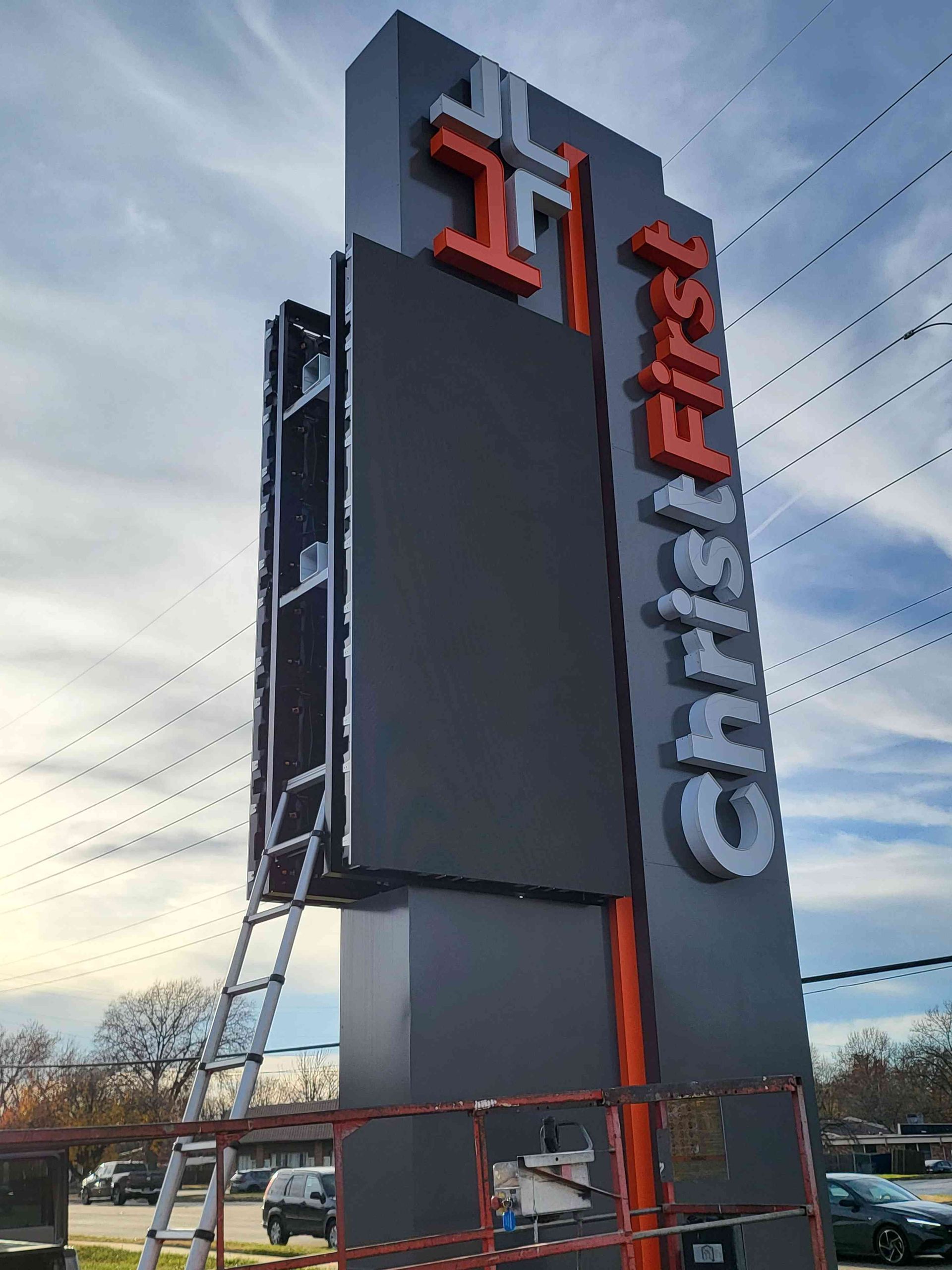 Church sign with LED screen, Christ First text, orange accent, with ladder for maintenance.