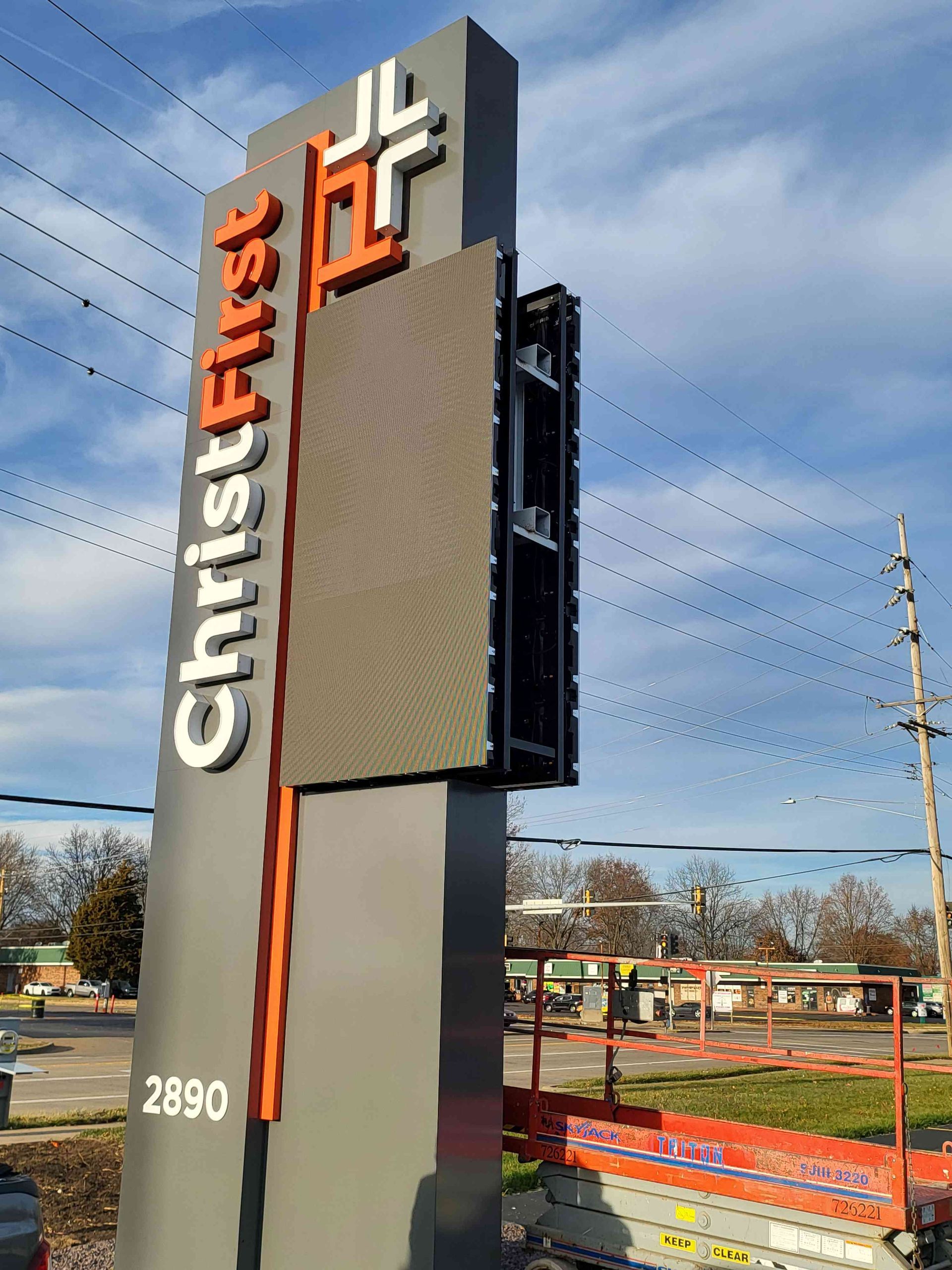 Christ First church sign with an LED screen, white text and orange accents, gray pole, and sunny day.