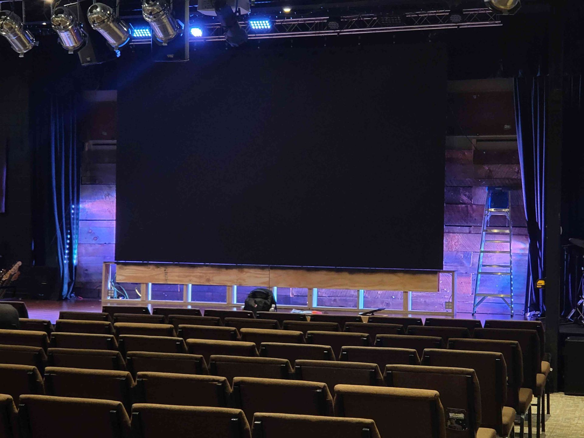 Empty theater stage with a large black screen and rows of seats.