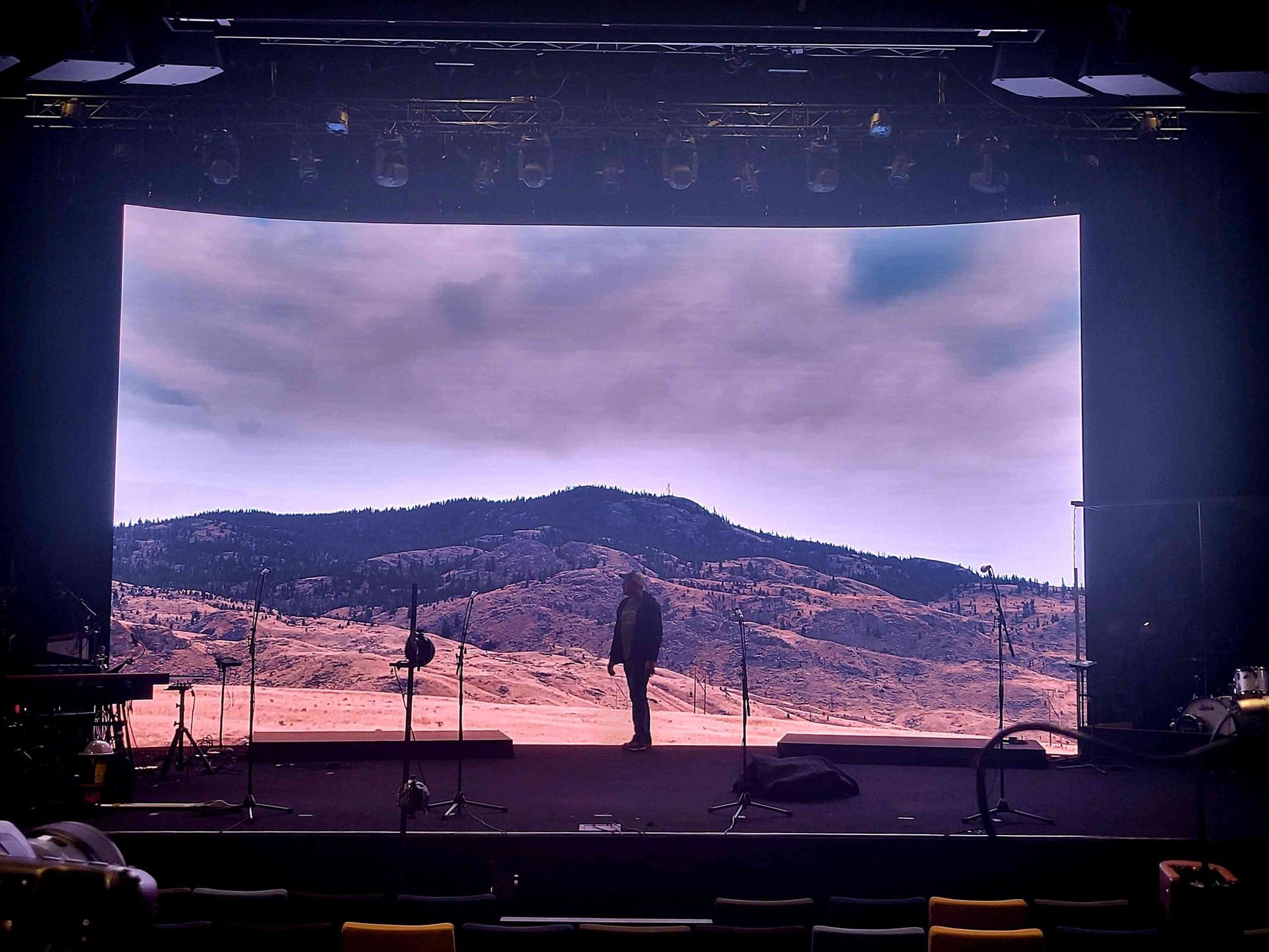 A person stands on a stage before a backdrop of a mountainous landscape.