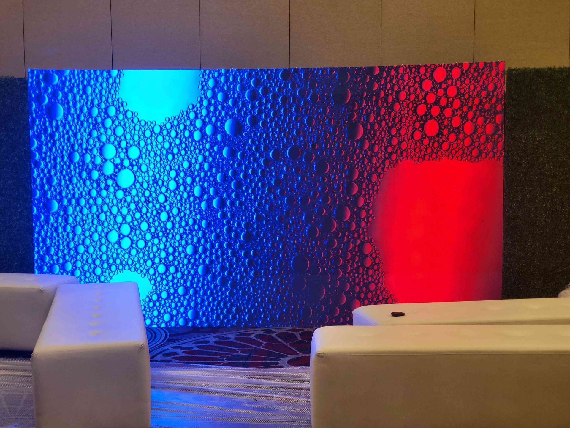 Blue and red illuminated wall with a bubble pattern; white seating in front.