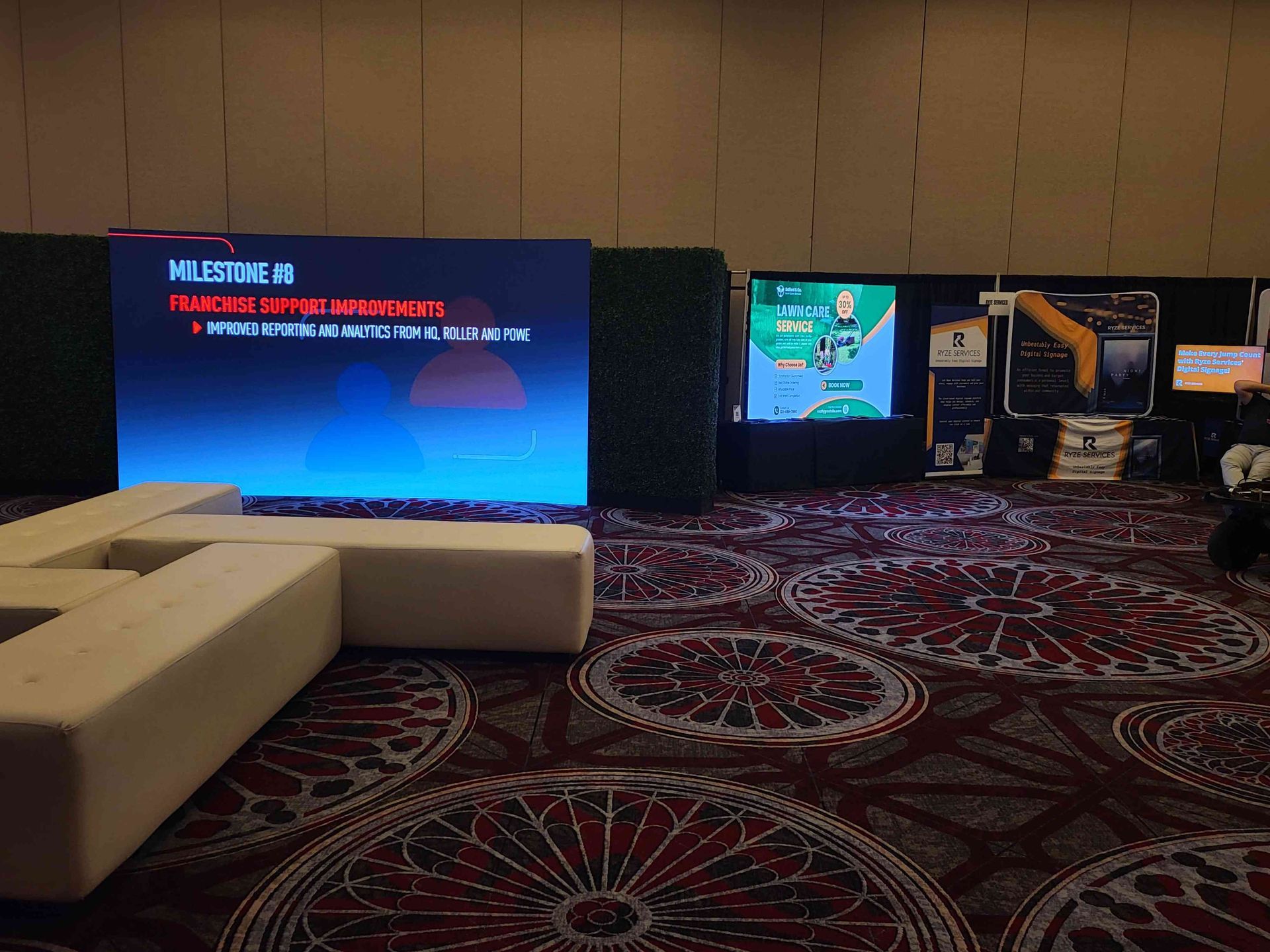 A conference room with screens displaying text, booths, and seating on patterned carpet.