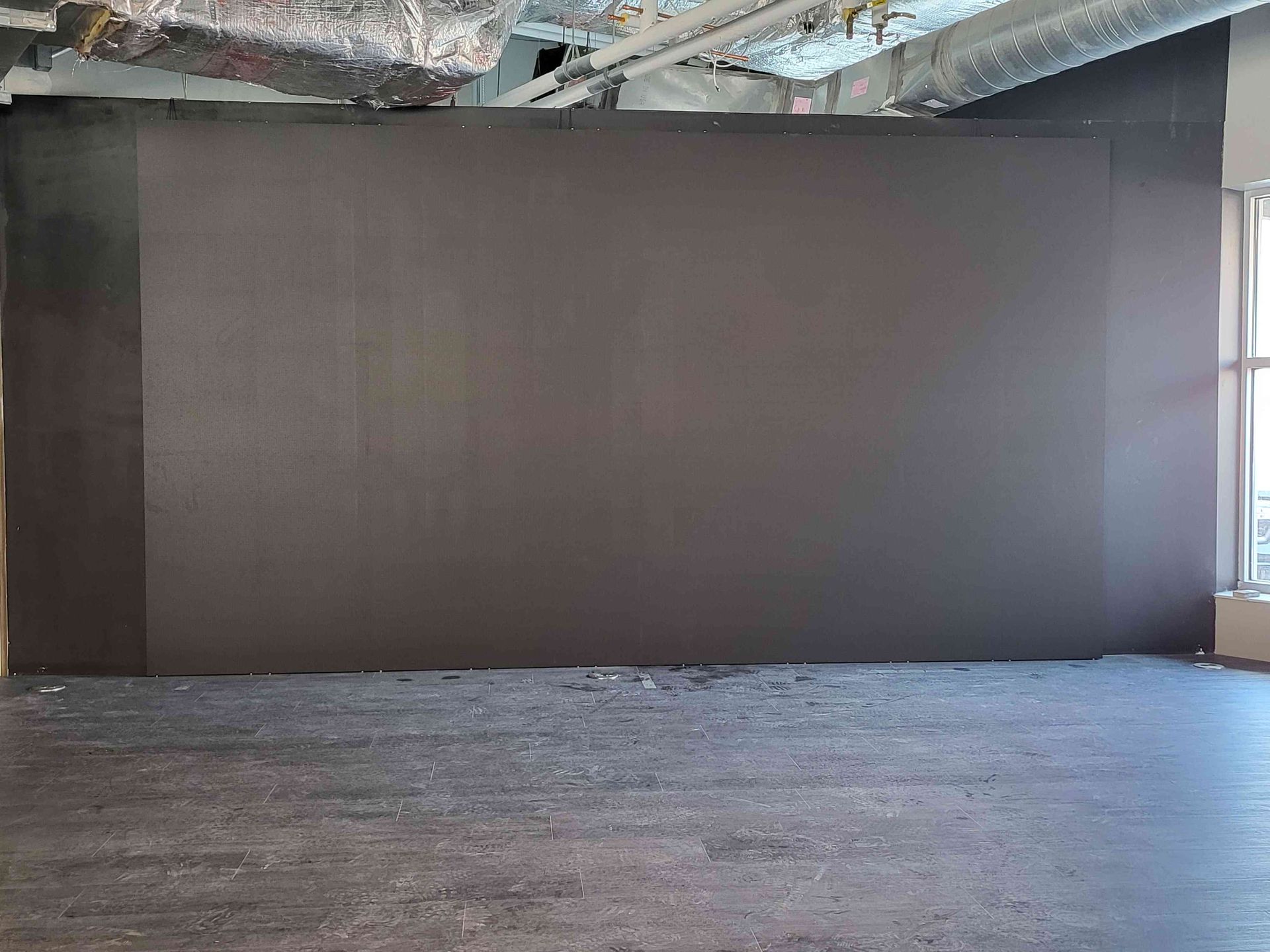 A large, empty, gray room with a dark gray wall and a window on the right.