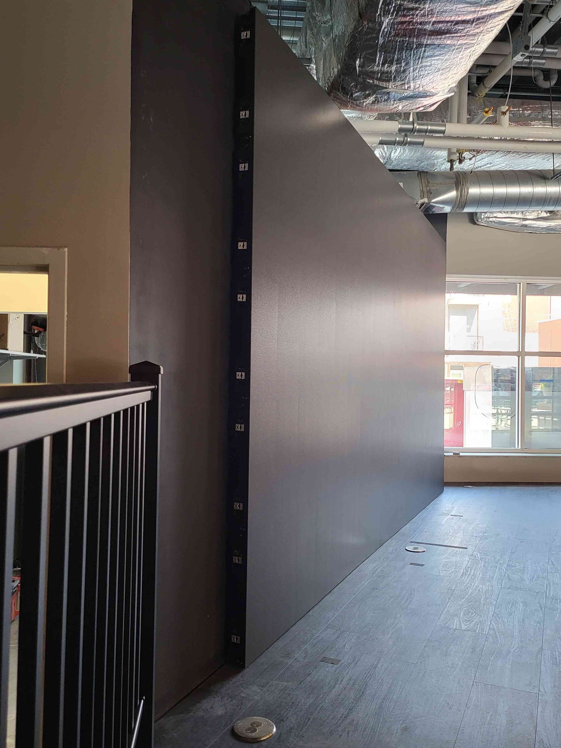 Dark gray angled wall with black markers, next to a black railing, in a brightly lit indoor space.